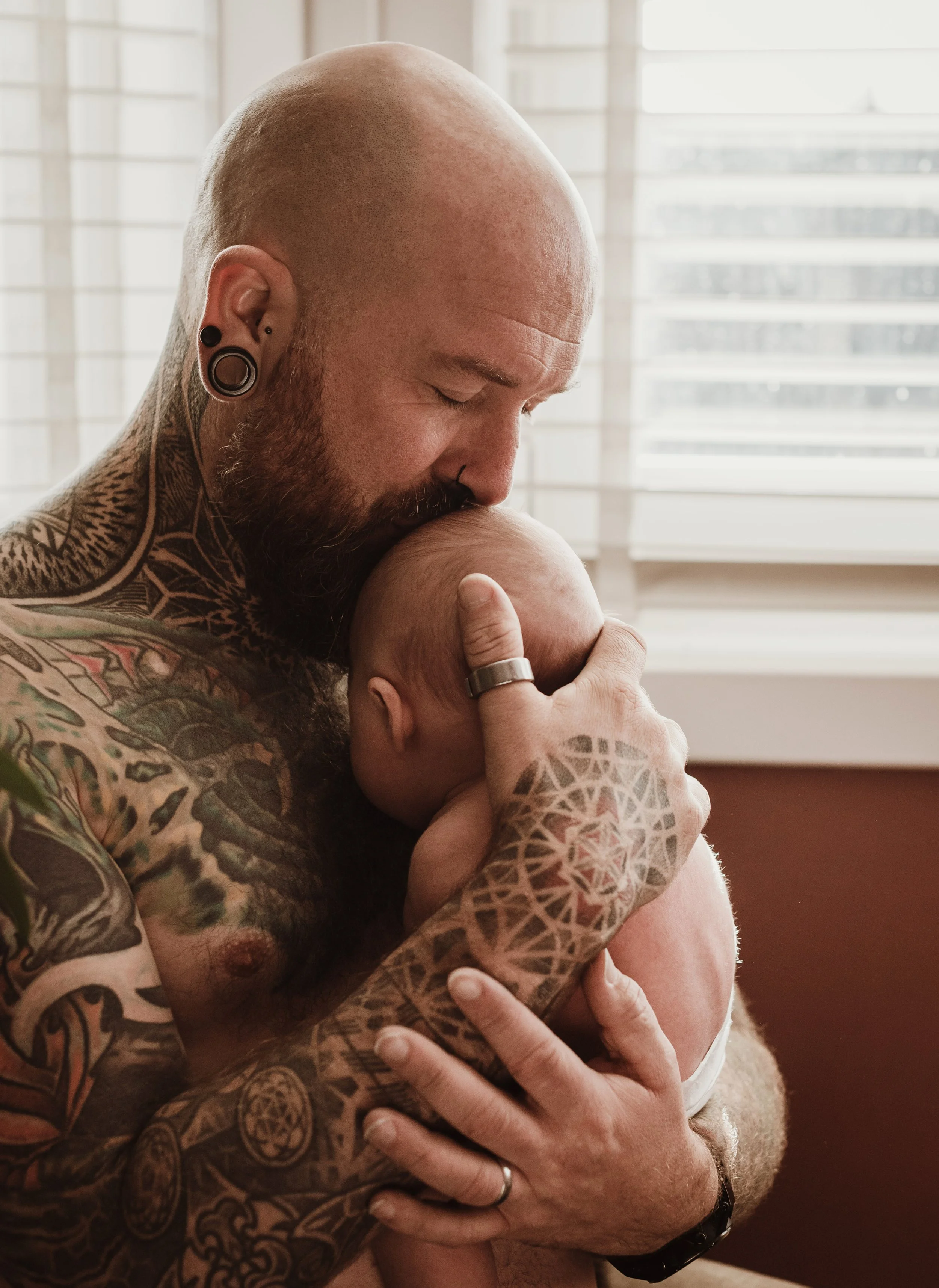 Tattooed father holding his newborn close with eyes closed in a tender moment during an at-home newborn photography session in Glasgow with Marieke Captures Birth