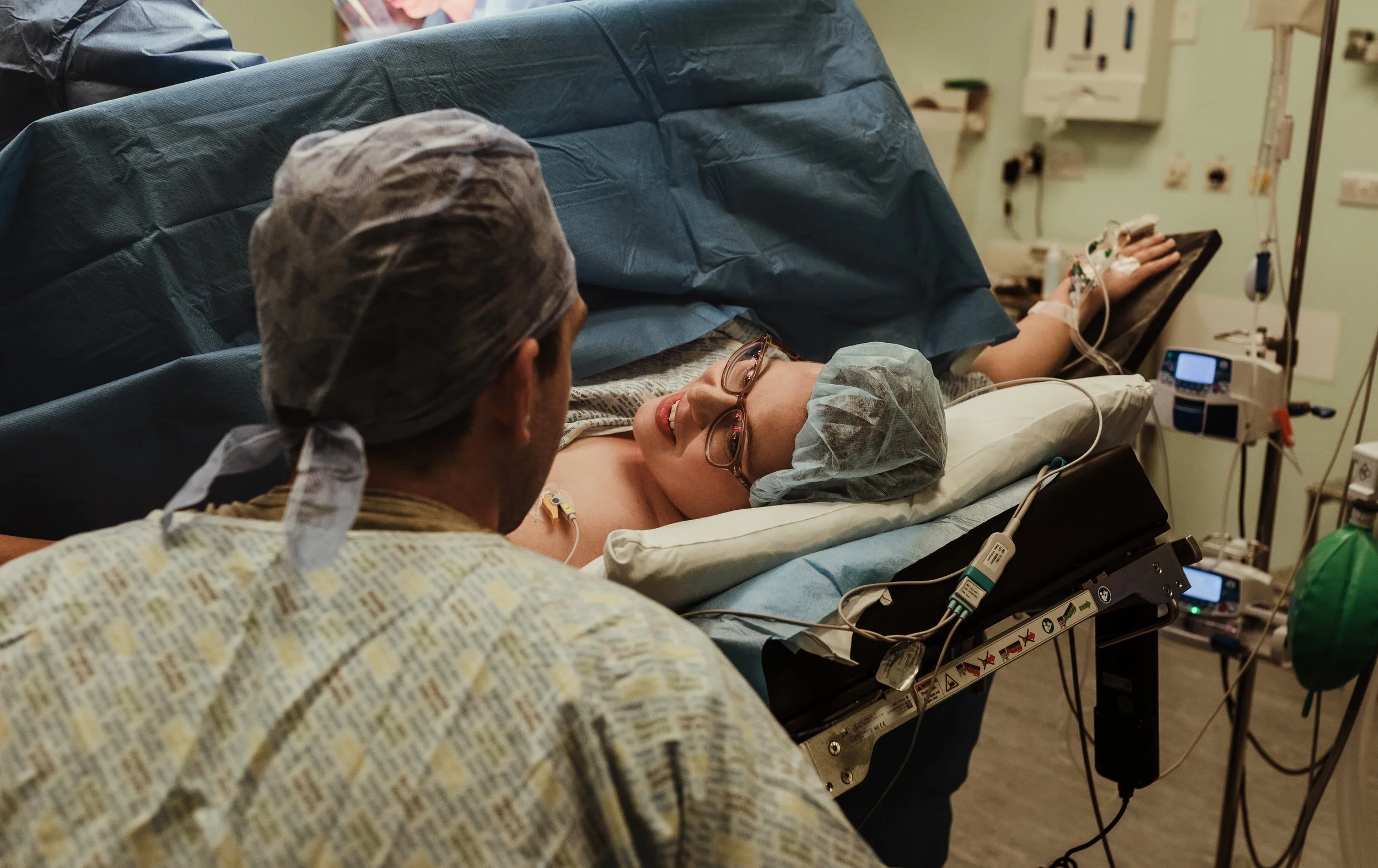 Couple fully prepped for surgery exchanging an excited look at each other in the moments before their caesarean birth at Princess Royal Maternity Hospital Glasgow
