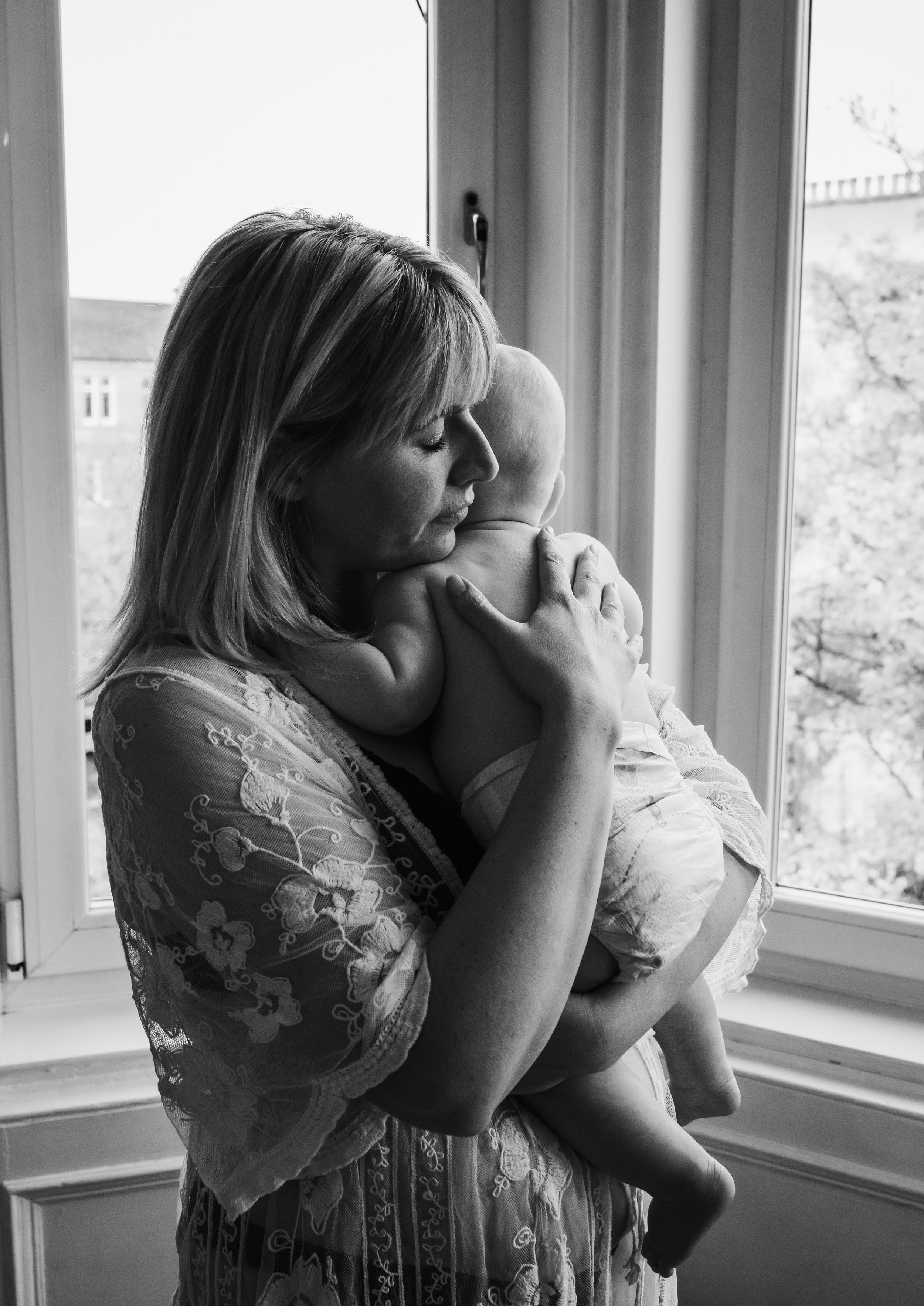 Black and white portrait of mother holding her newborn by a window during an at-home newborn photography session in Scotland with Marieke Captures Birth