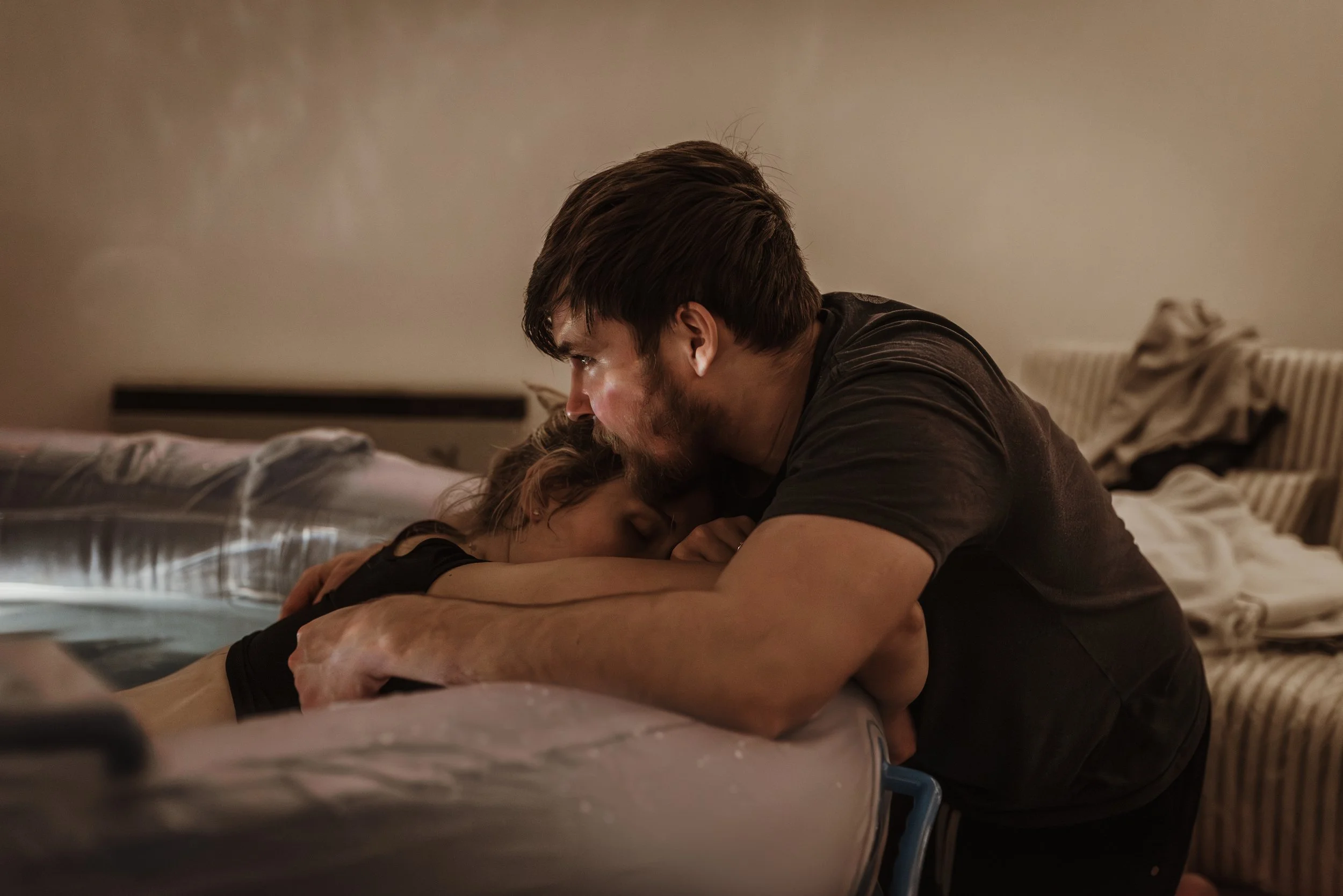 Husband embracing his wife during active labour at their home birth in Glasgow, offering physical and emotional support as contractions intensify.