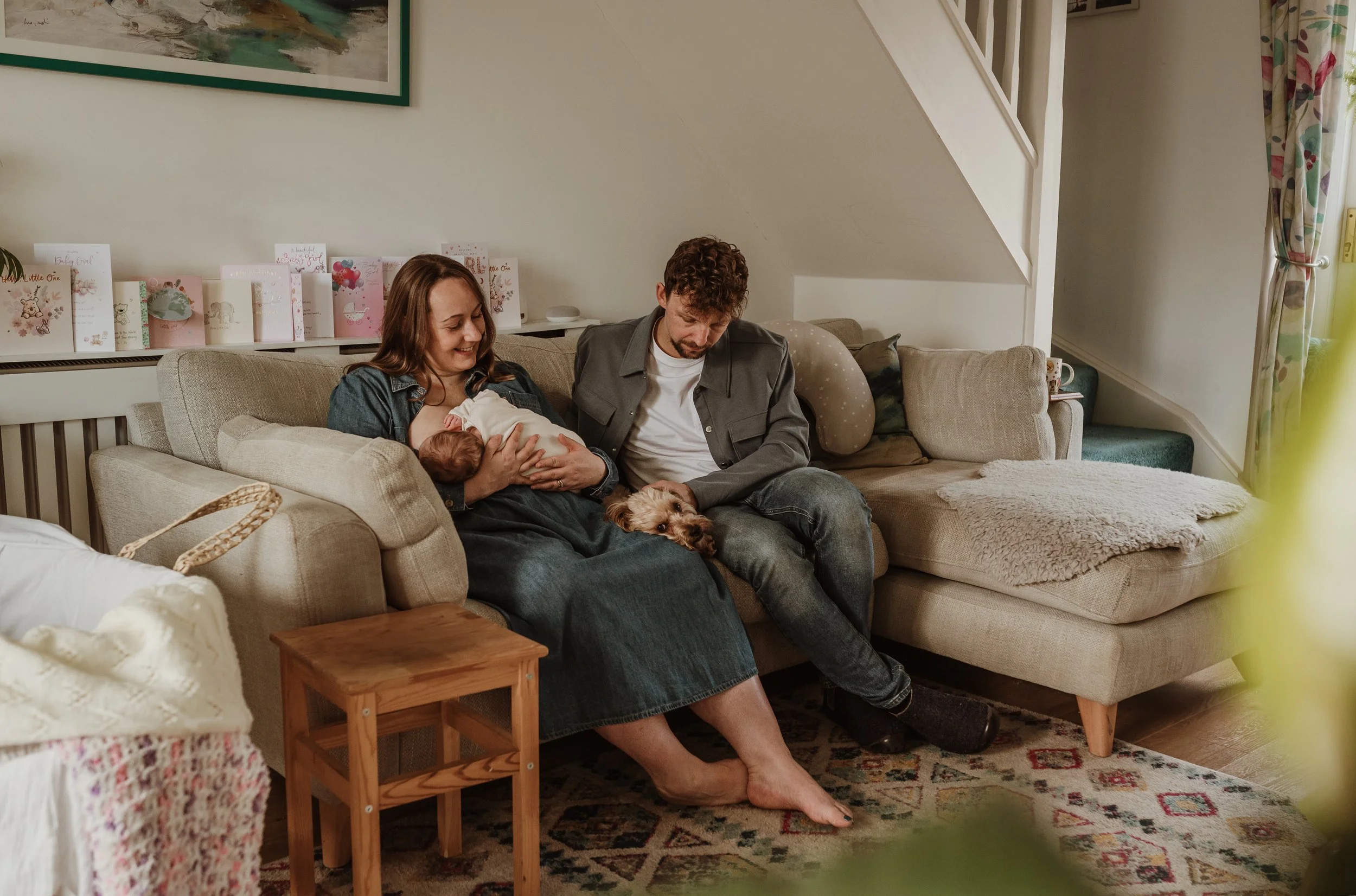 New family of three sitting together on a sofa with their dog during an at-home newborn photography session in Glasgow with Marieke Captures Birth