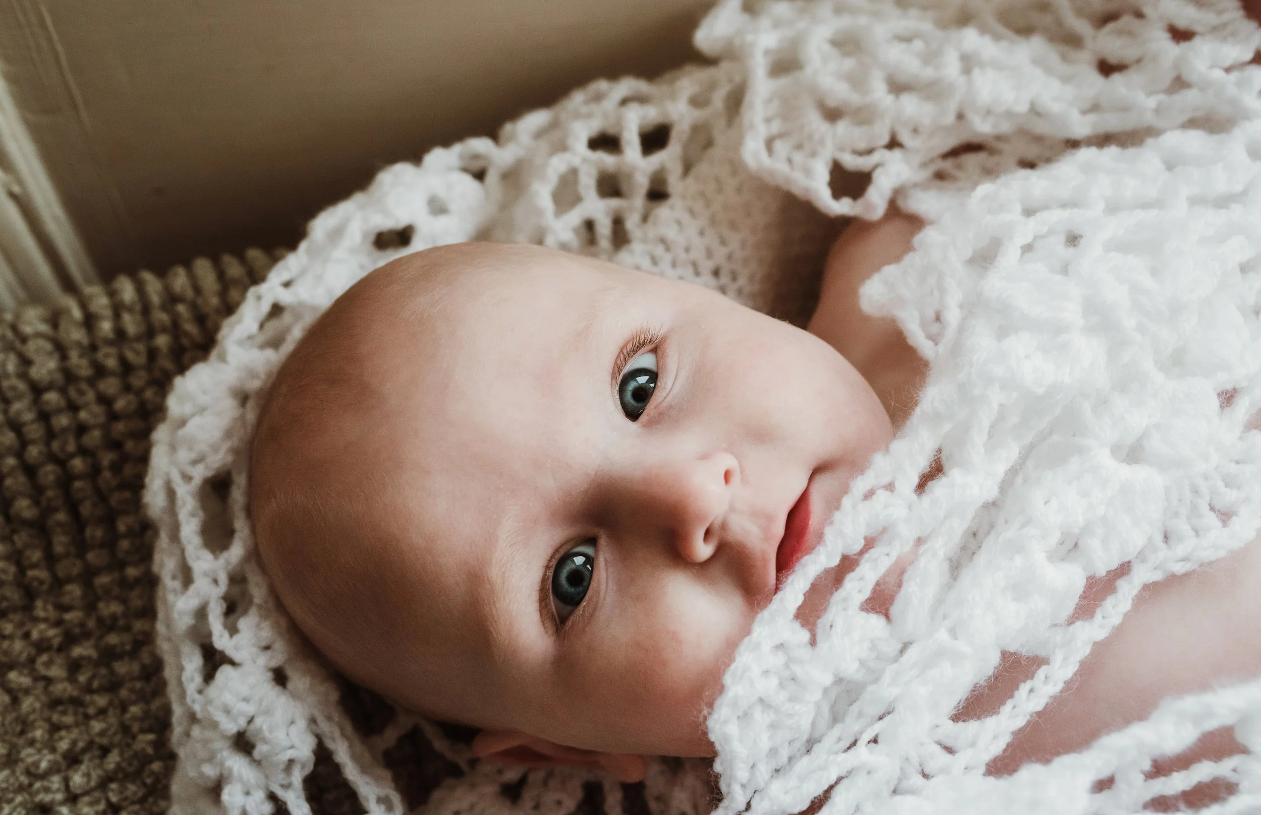 Close up of newborn baby looking upward wrapped in a delicate lace blanket during a newborn photography session with Glasgow photographer Marieke Captures Birth