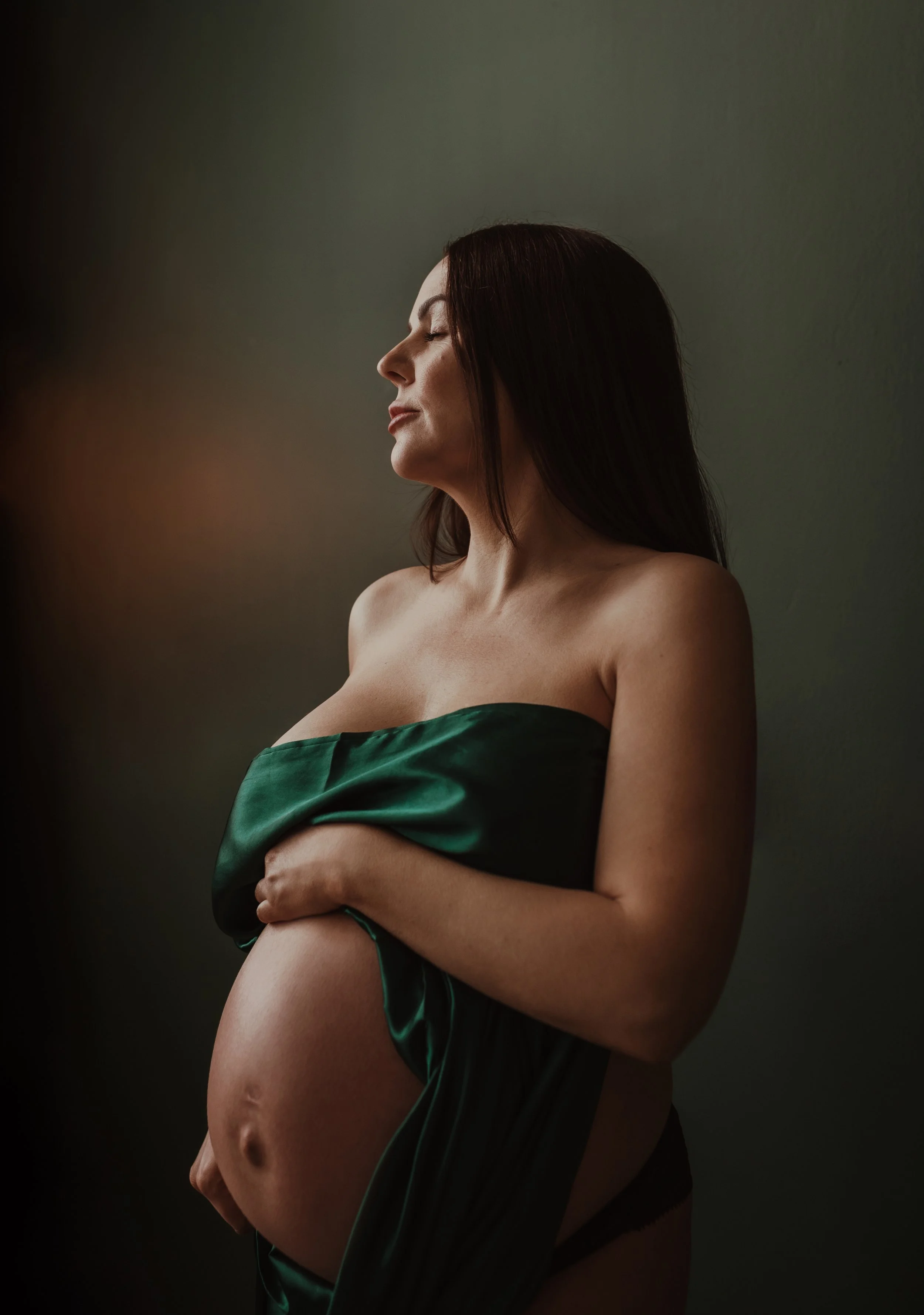 Pregnant woman in green satin drape looking upward during a studio maternity portrait session with Marieke Captures Birth in Glasgow