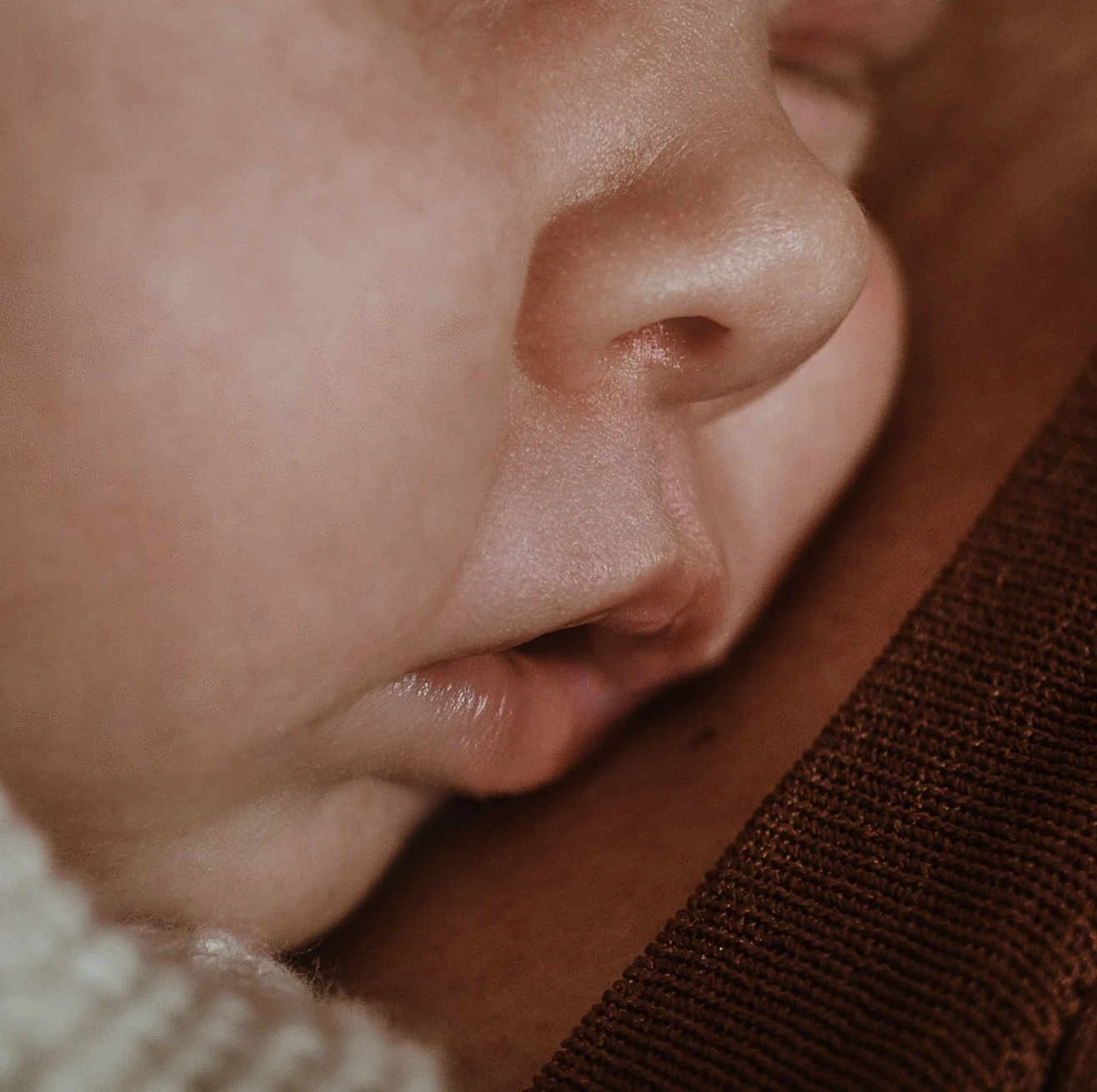 Close up of newborn baby's face in soft peachy tones during a newborn photography session with Glasgow photographer Marieke Captures Birth