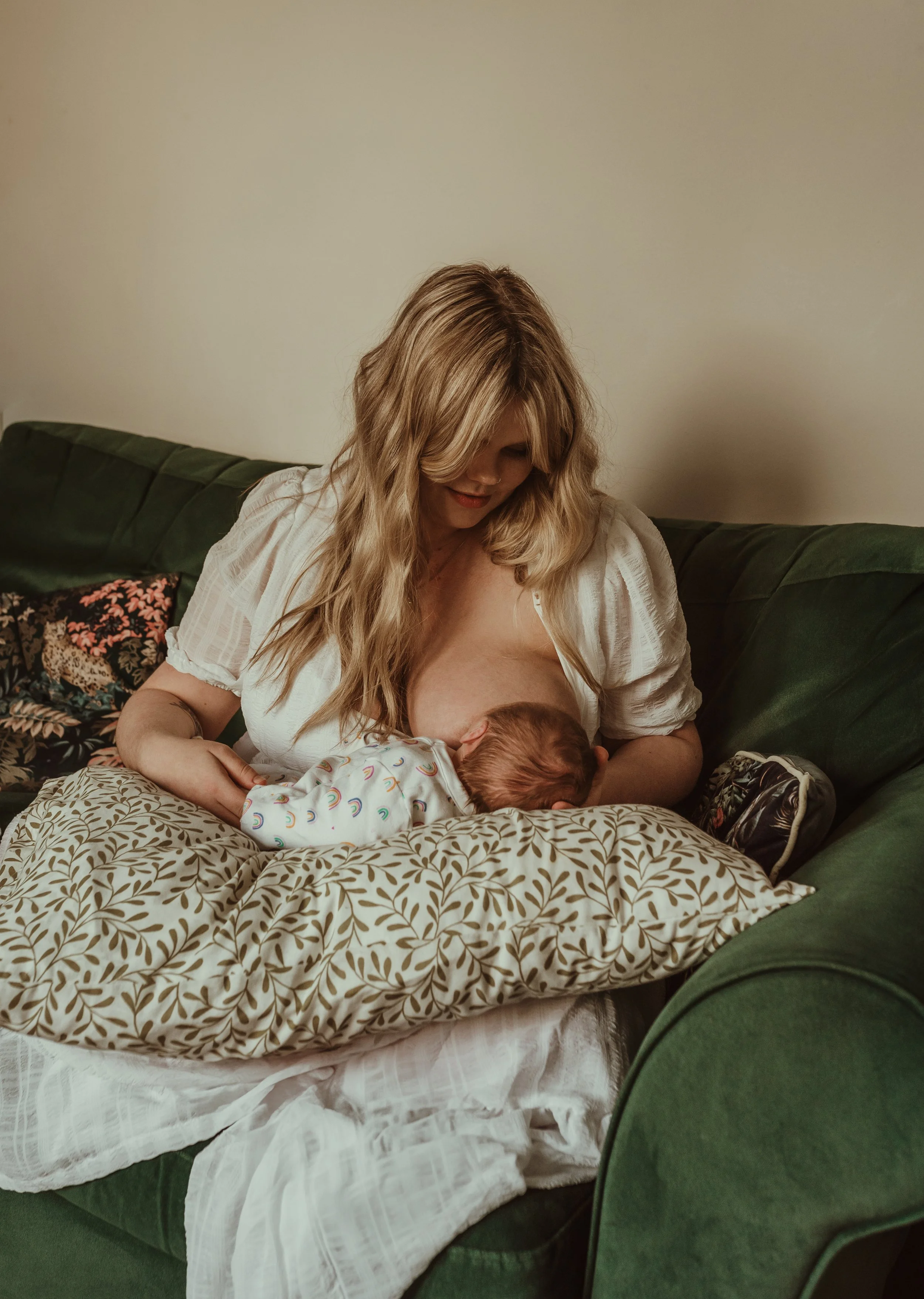 Mother nursing her newborn in natural light on a green sofa during a relaxed at-home newborn photography session in Scotland with Marieke Captures Birth