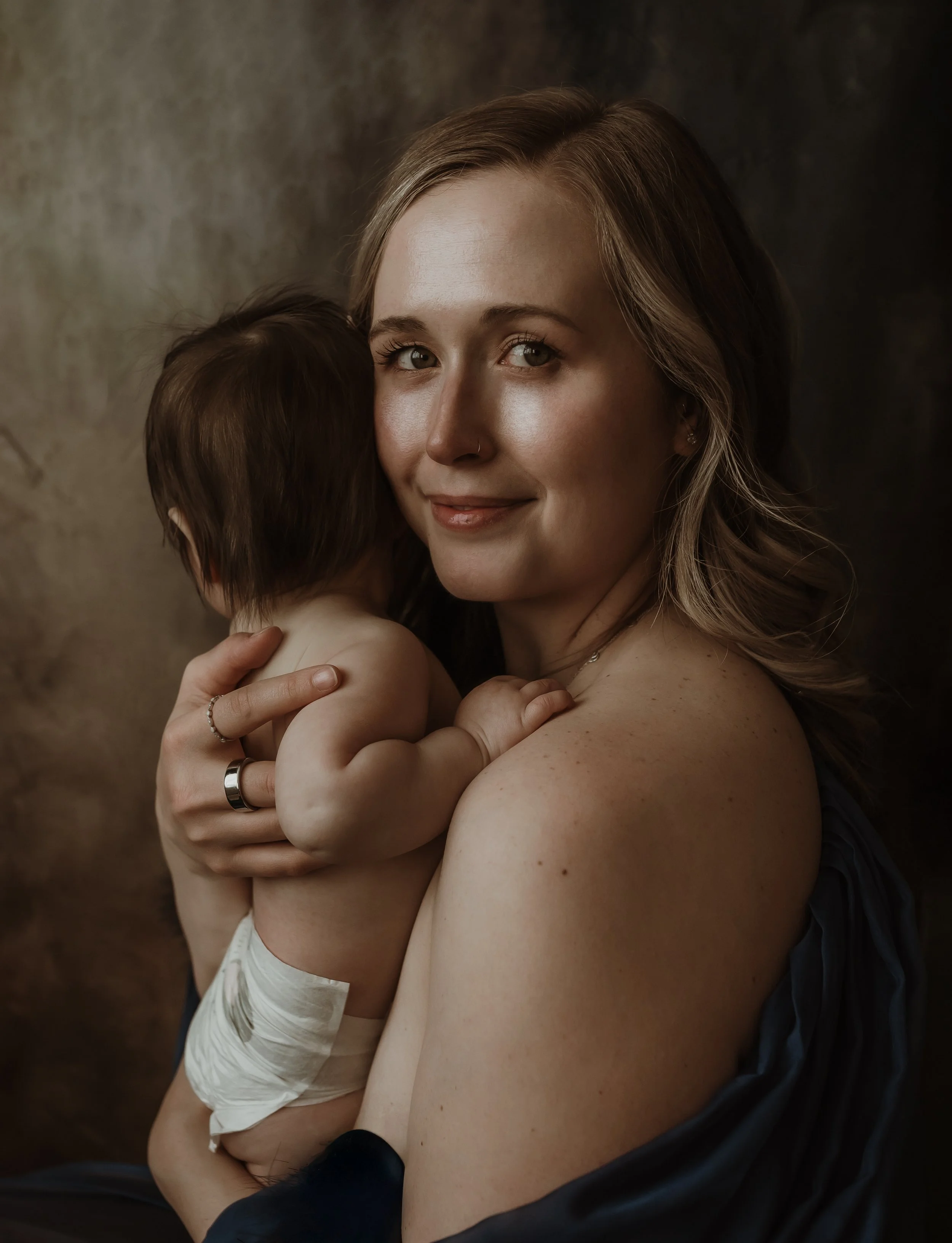 Studio portrait of a mother smiling warmly while holding her baby during a nursing photography session with Glasgow photographer Marieke Captures Birth
