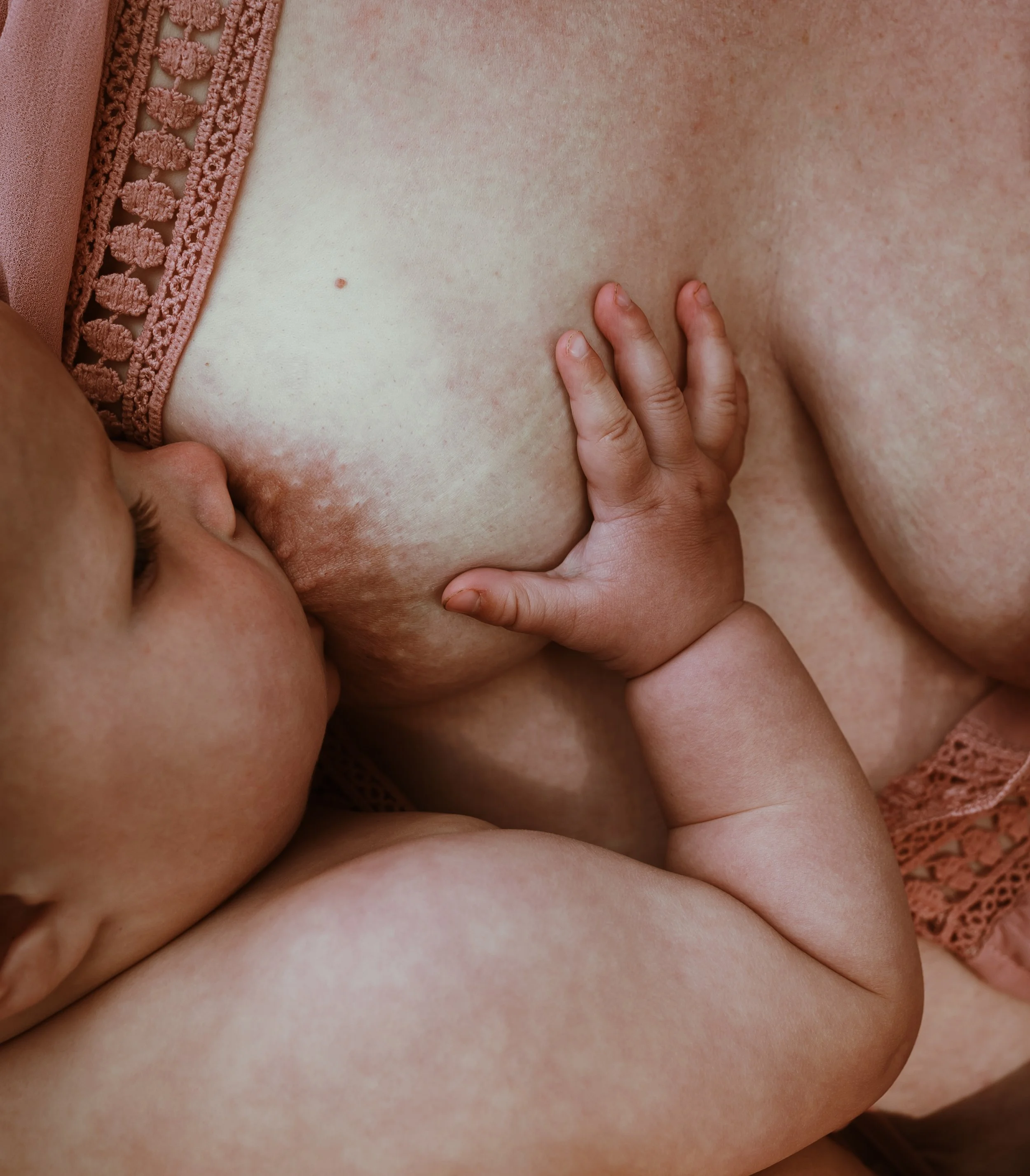 Close up of breastfeeding in soft pink muslin with baby hands visible during a nursing photography session with Marieke Captures Birth Scotland
