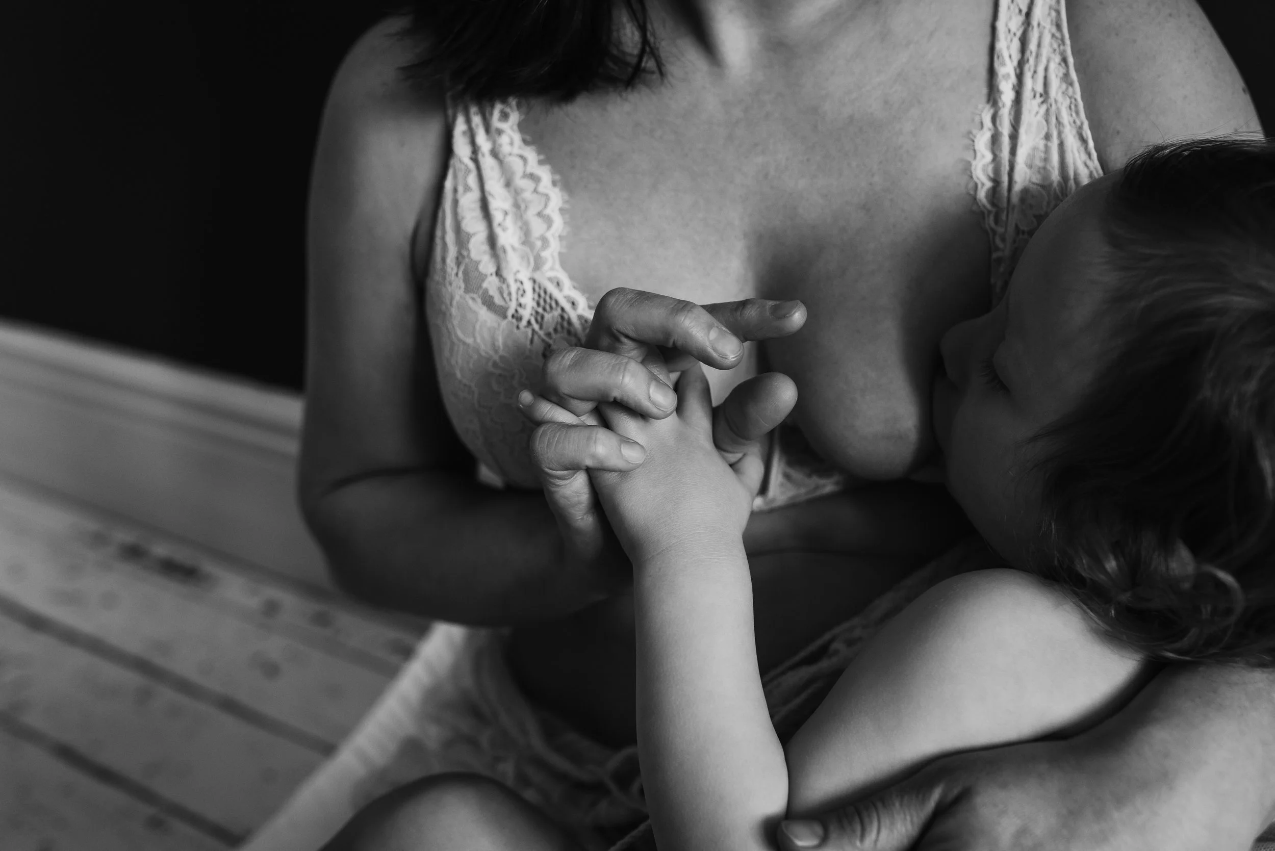 Mother nursing her toddler while seated indoors in a white lace gown during a nursing photography session with Glasgow photographer Marieke Captures Birth