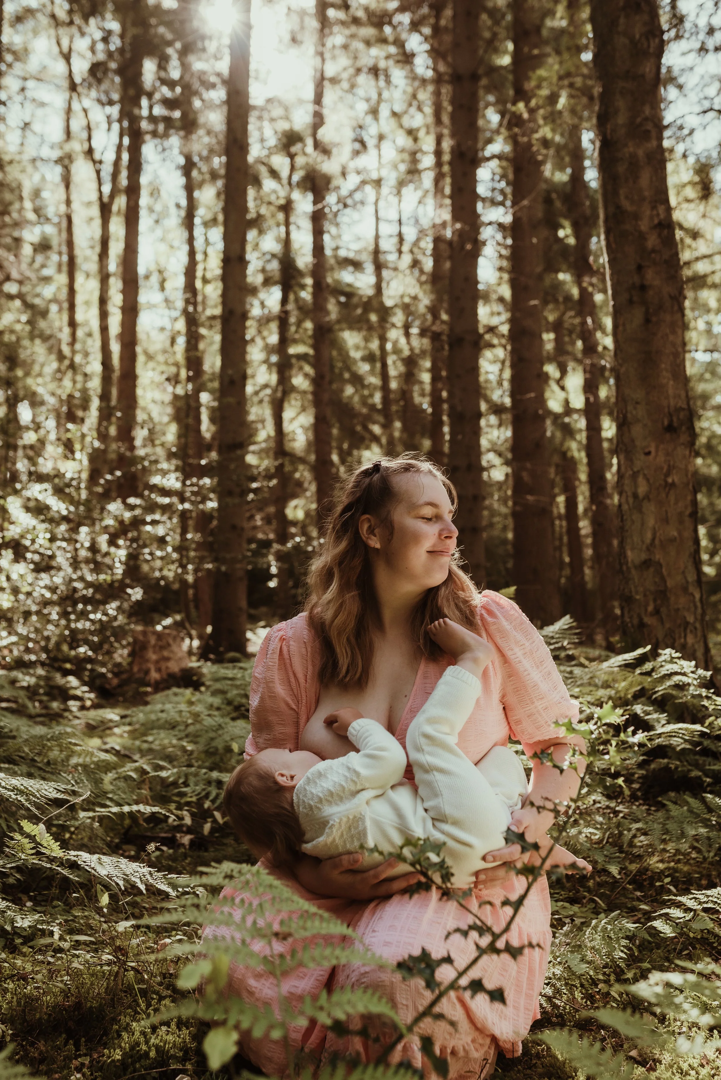 Mother nursing her toddler outdoors in a pink dress during an outdoor nursing photography session in Scotland with Marieke Captures Birth
