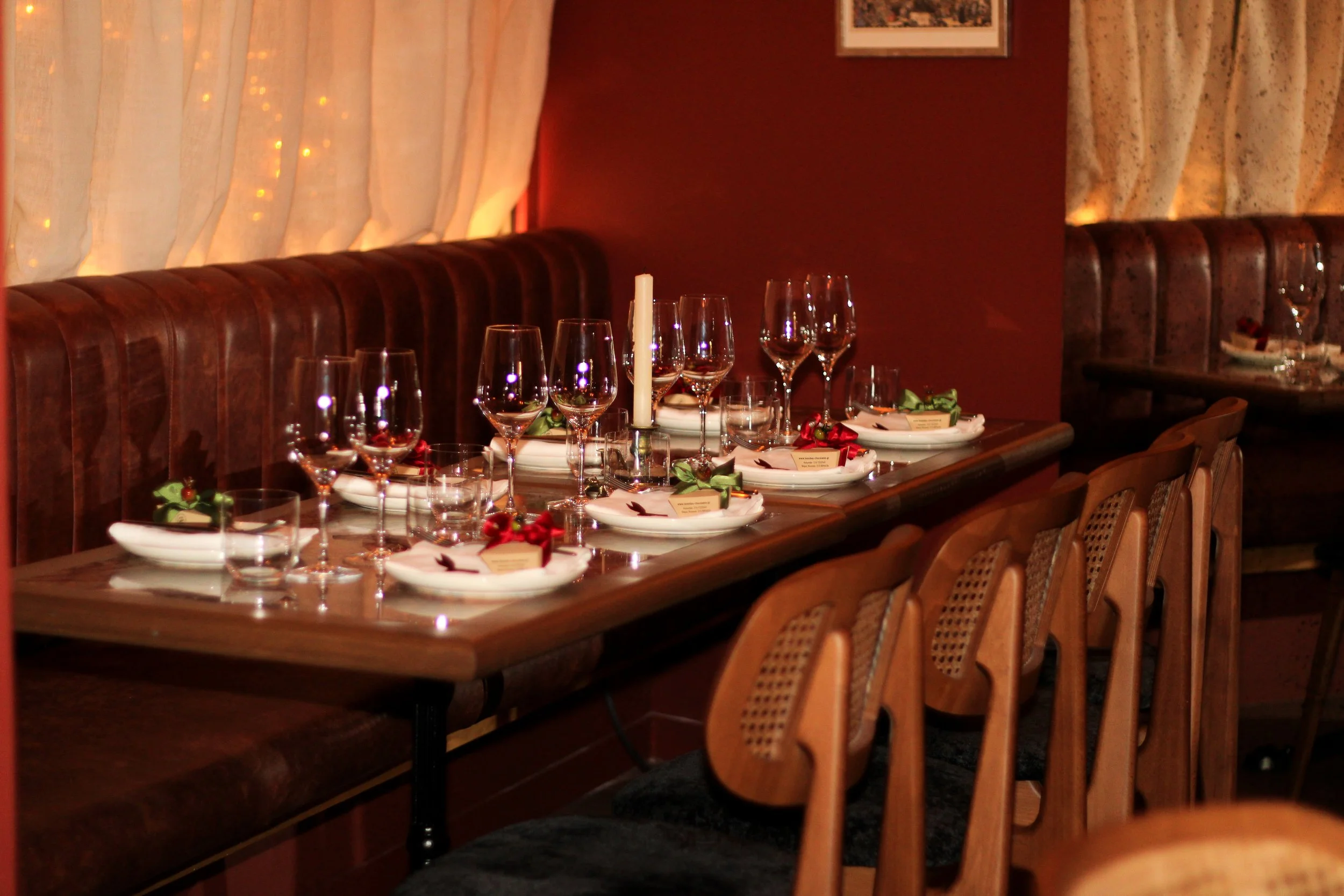 A restaurant table set for a holiday dinner, with wine glasses, plates, candles, and festive decorations.