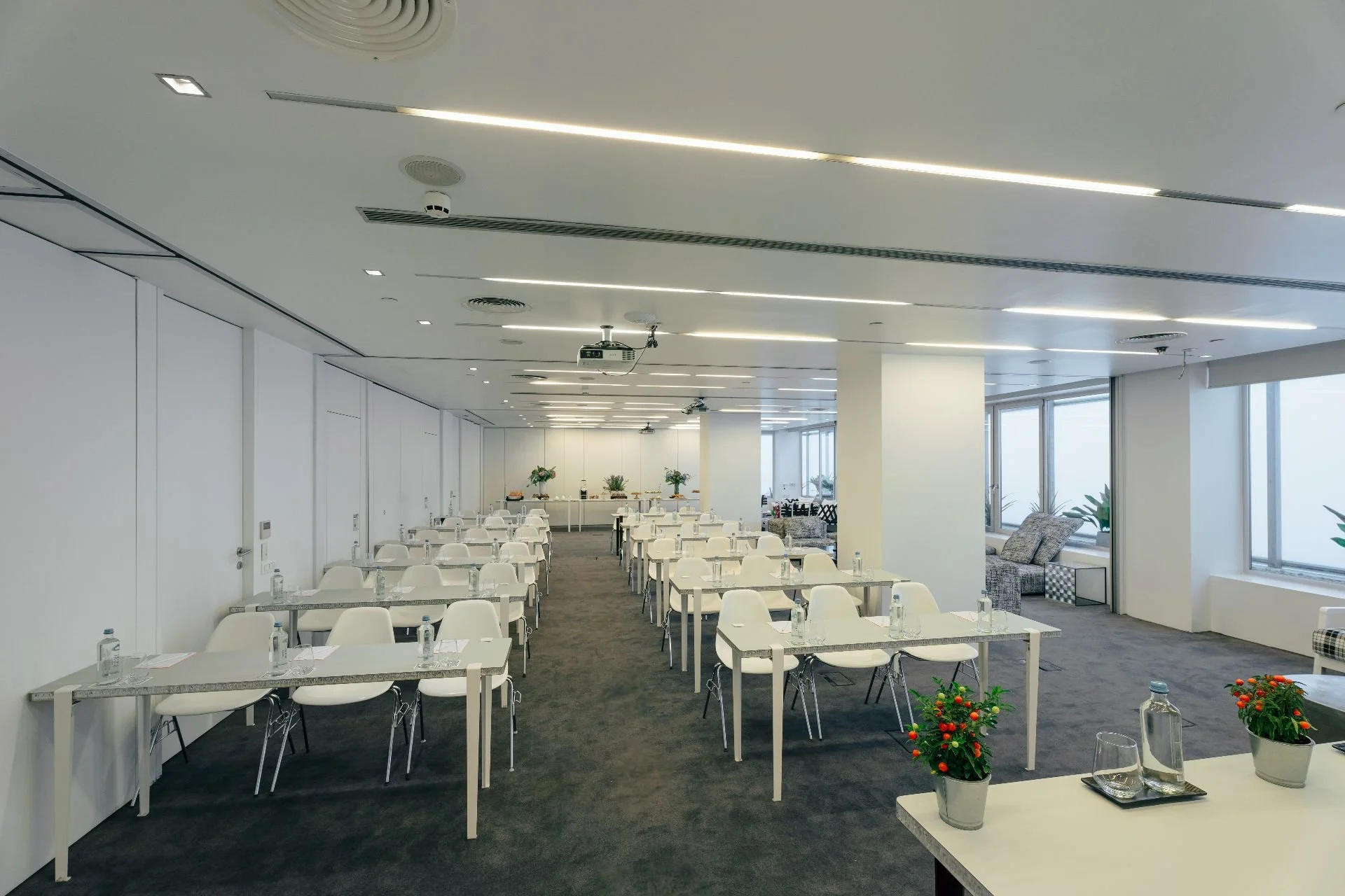 Conference room set up for a meeting with white tables and chairs, bottles of water, glasses, and plants on the tables, with large windows and a modern design.