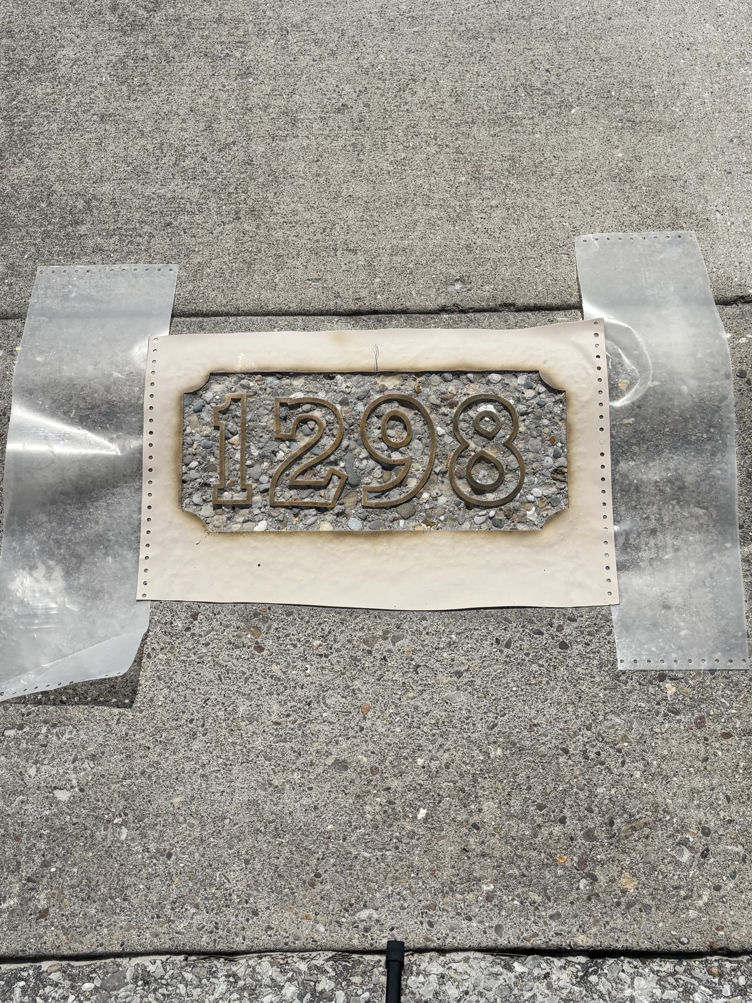 Image of curb with stencil and sandblasted address numbers in progress, showing the recessed etching process for durable curb address markings.