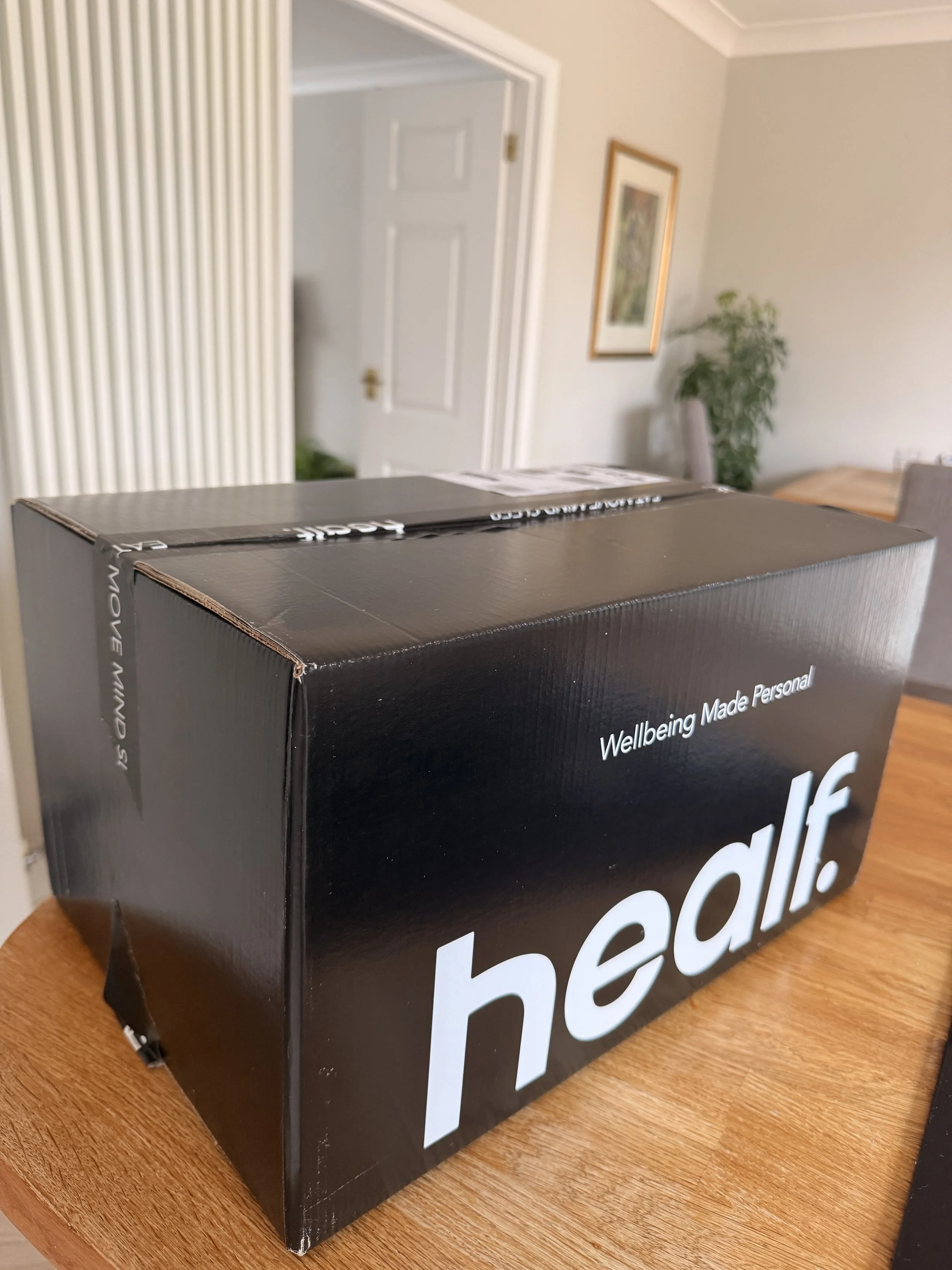 A black cardboard box on a wooden table with the word 'health' written in large white letters, along with the phrase 'Wellbeing Made Personal' on the side.