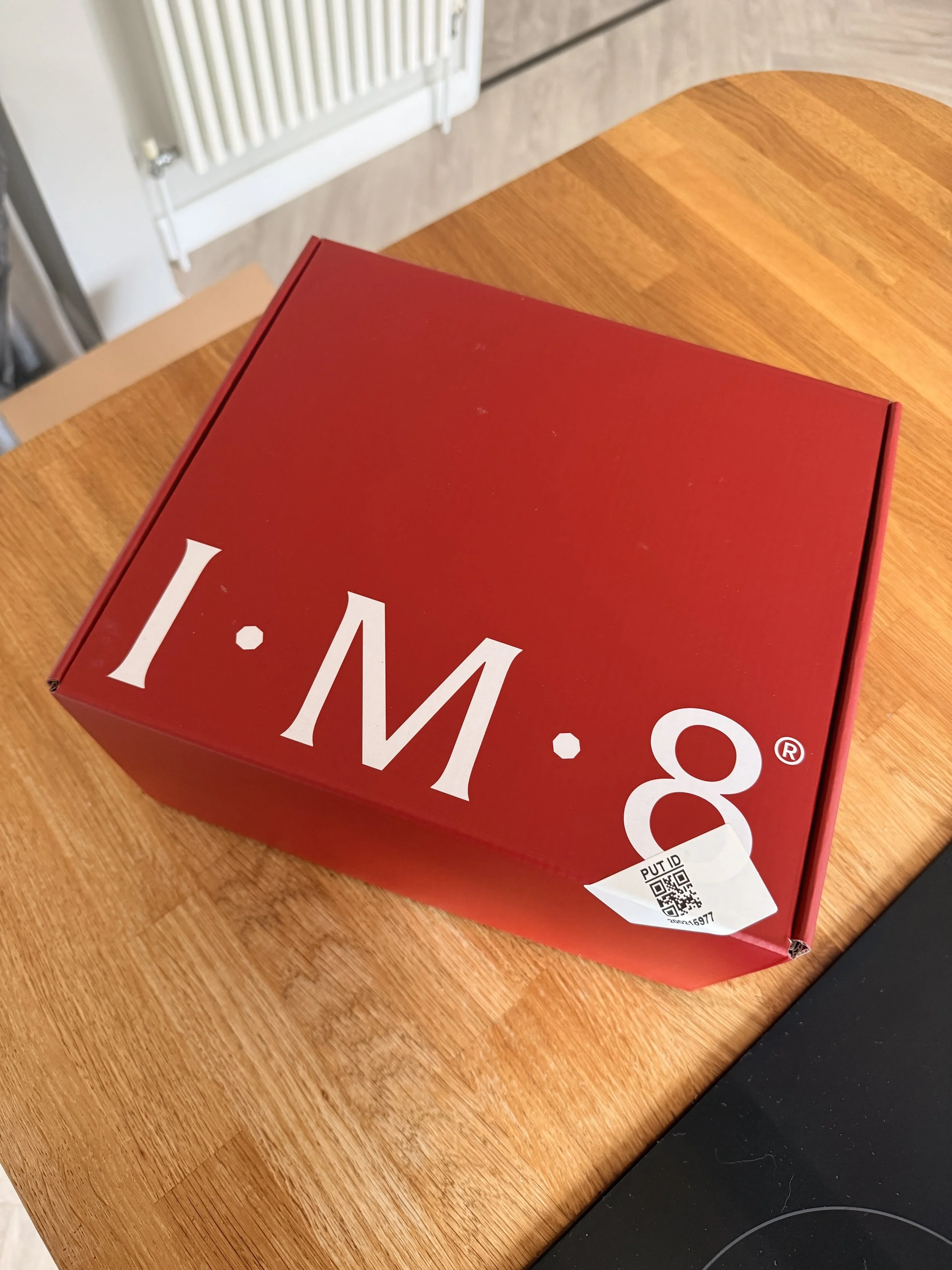 Close-up of a red cardboard pizza box on a wooden table, with a white barcode sticker and QR code on the side.