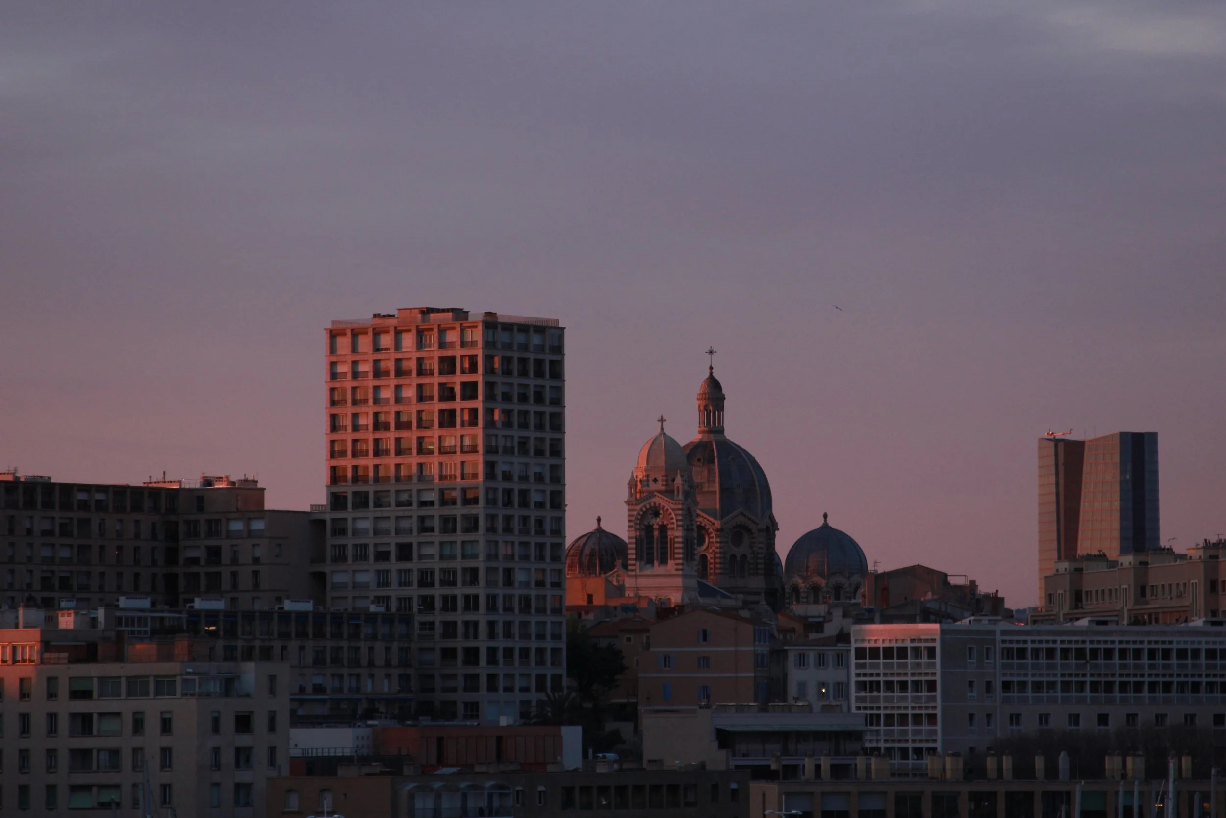 City skyline at sunset with modern high-rise buildings and a historic domed church in the center.