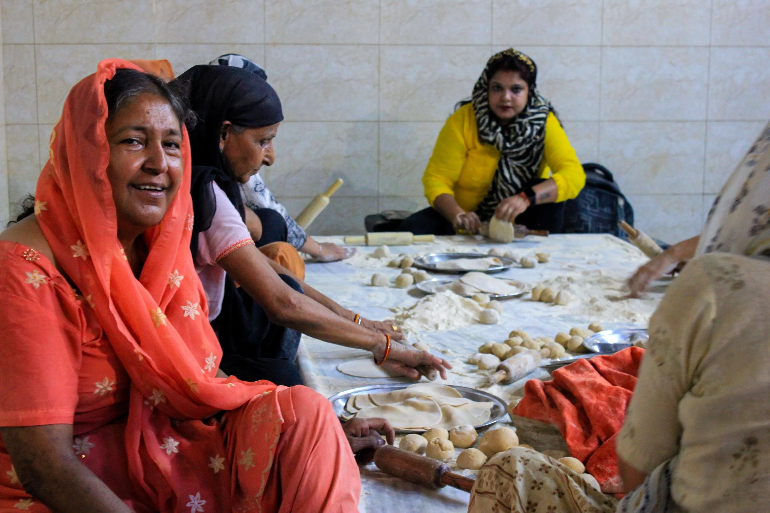Women and a girl making traditional bread together on a low table, rolling dough into small balls.