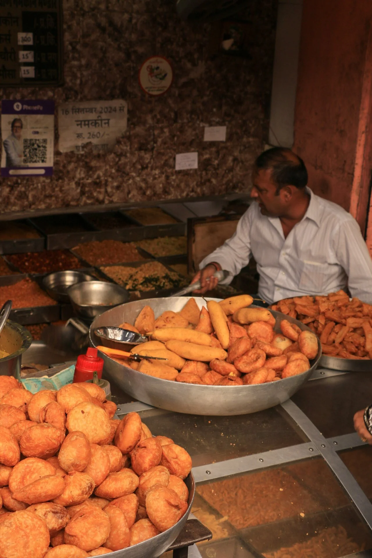 A street food vendor preparing various fried snacks at a market stall.