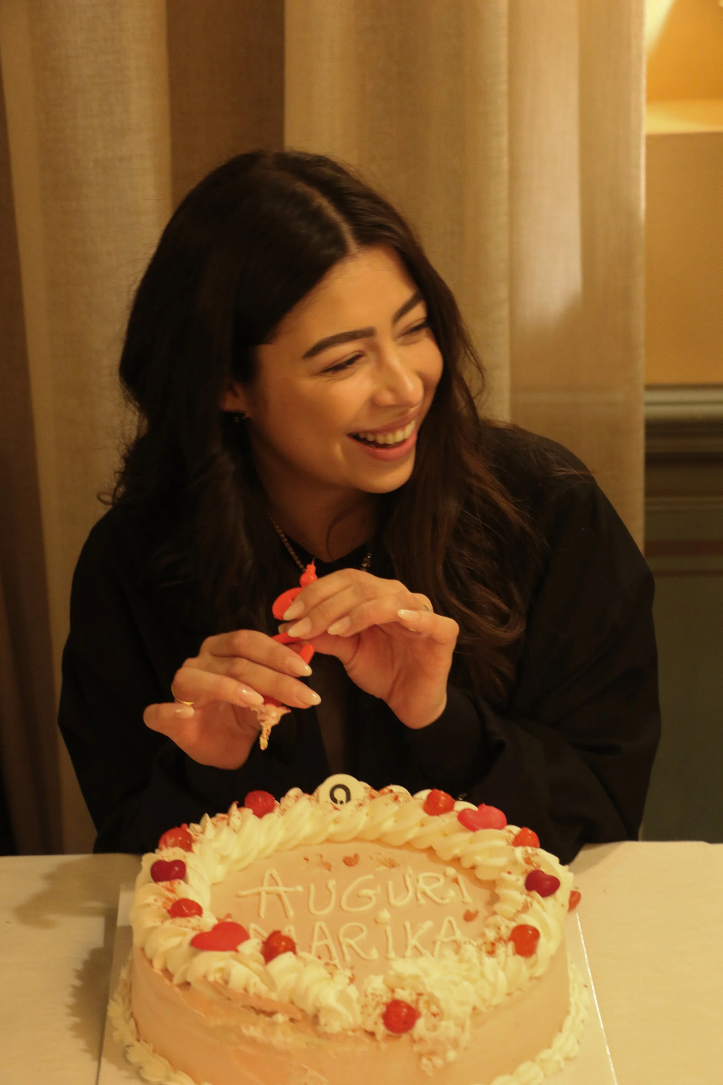 Woman smiling at a birthday cake with the message "Auguri Arika" written on it.