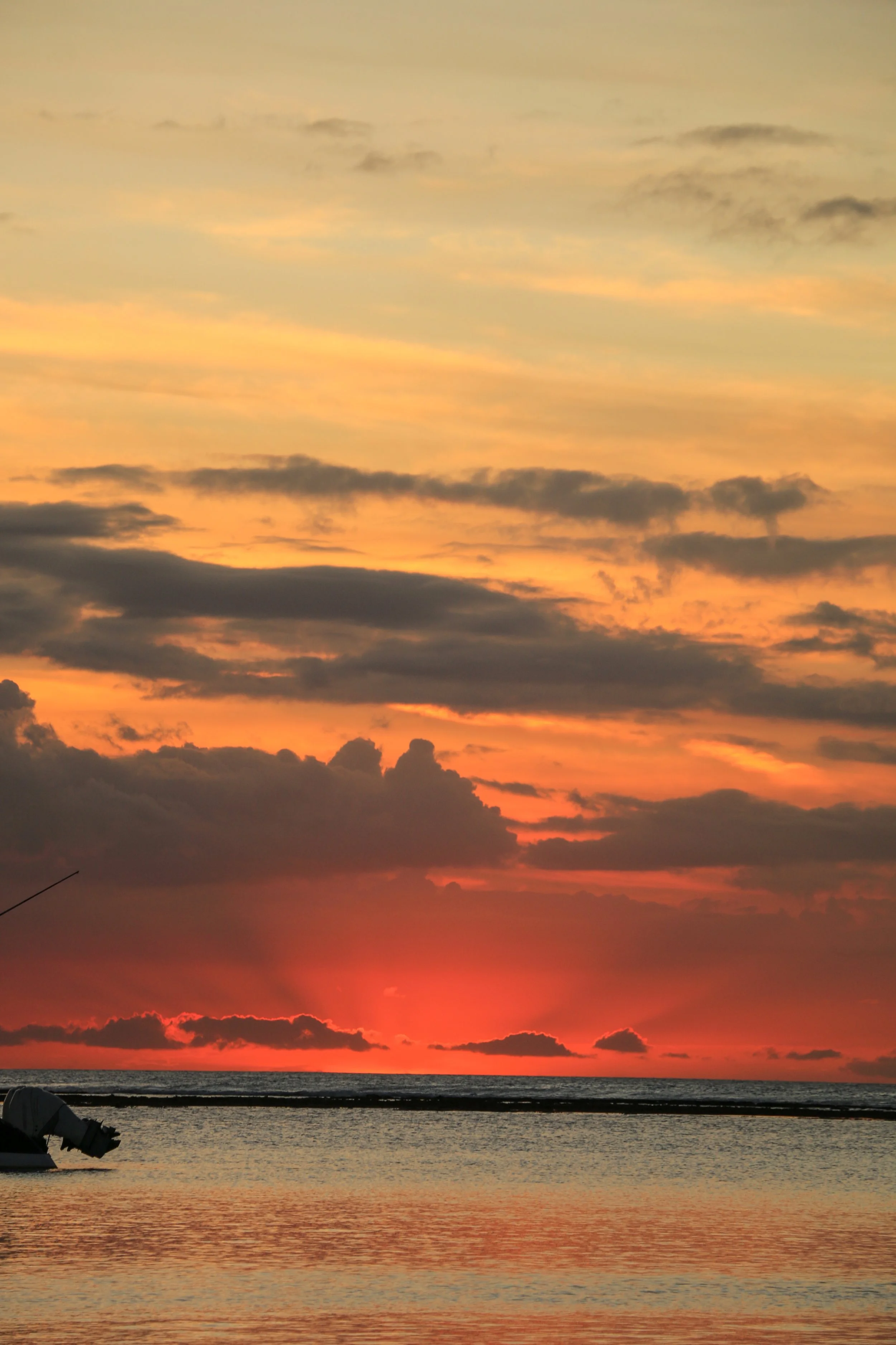 Sunset over the ocean with colorful clouds and a boat on the water.