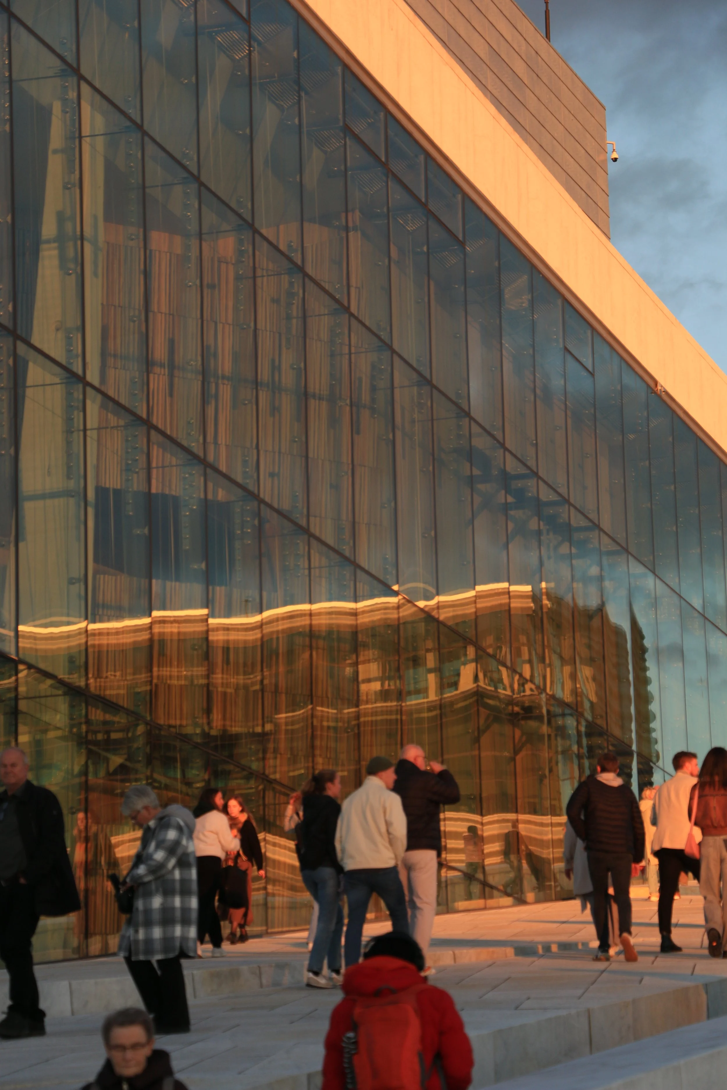 People walking outside a modern building with reflective glass windows at sunset.