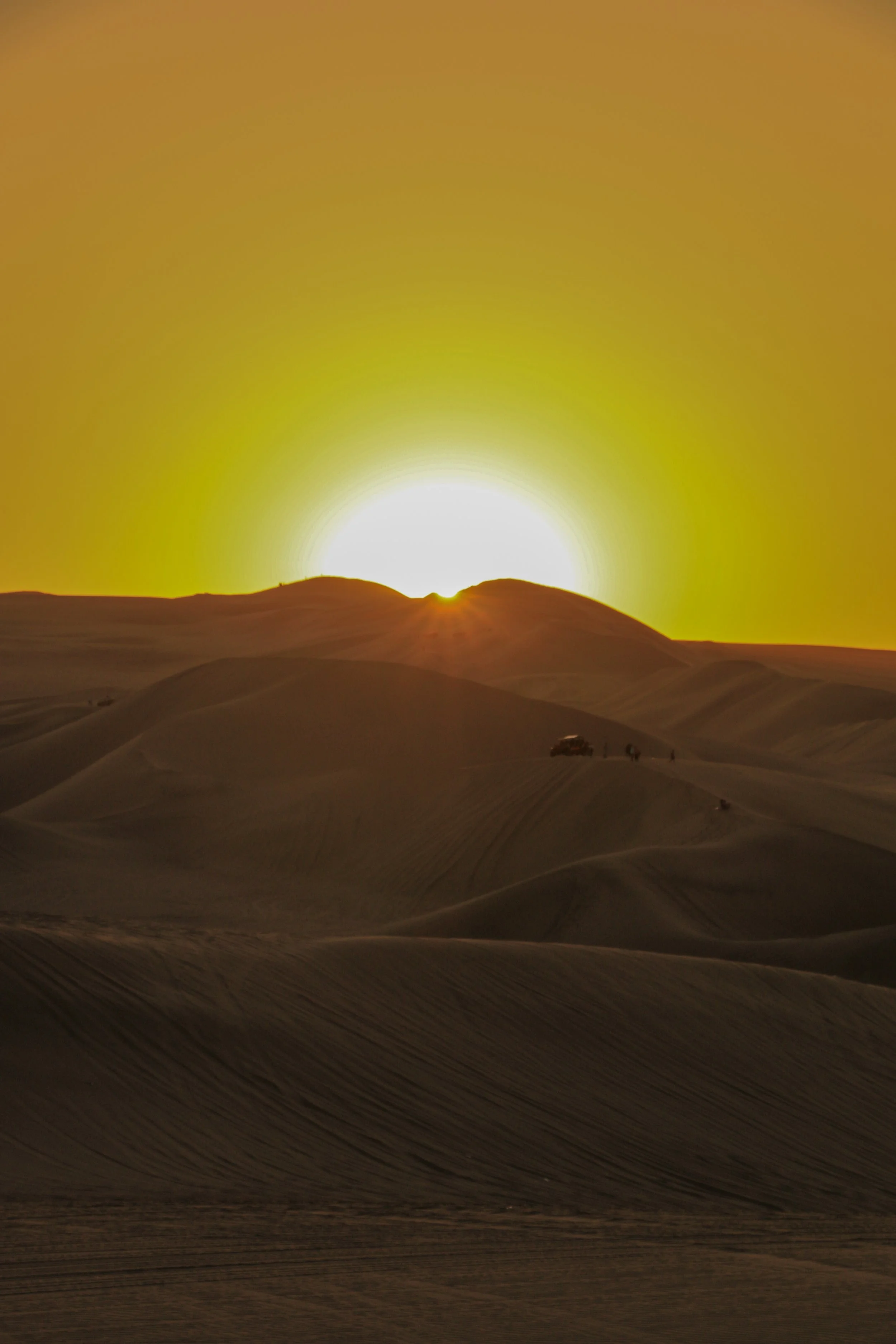 Sun setting over sand dunes in a desert with a gradient yellow sky.