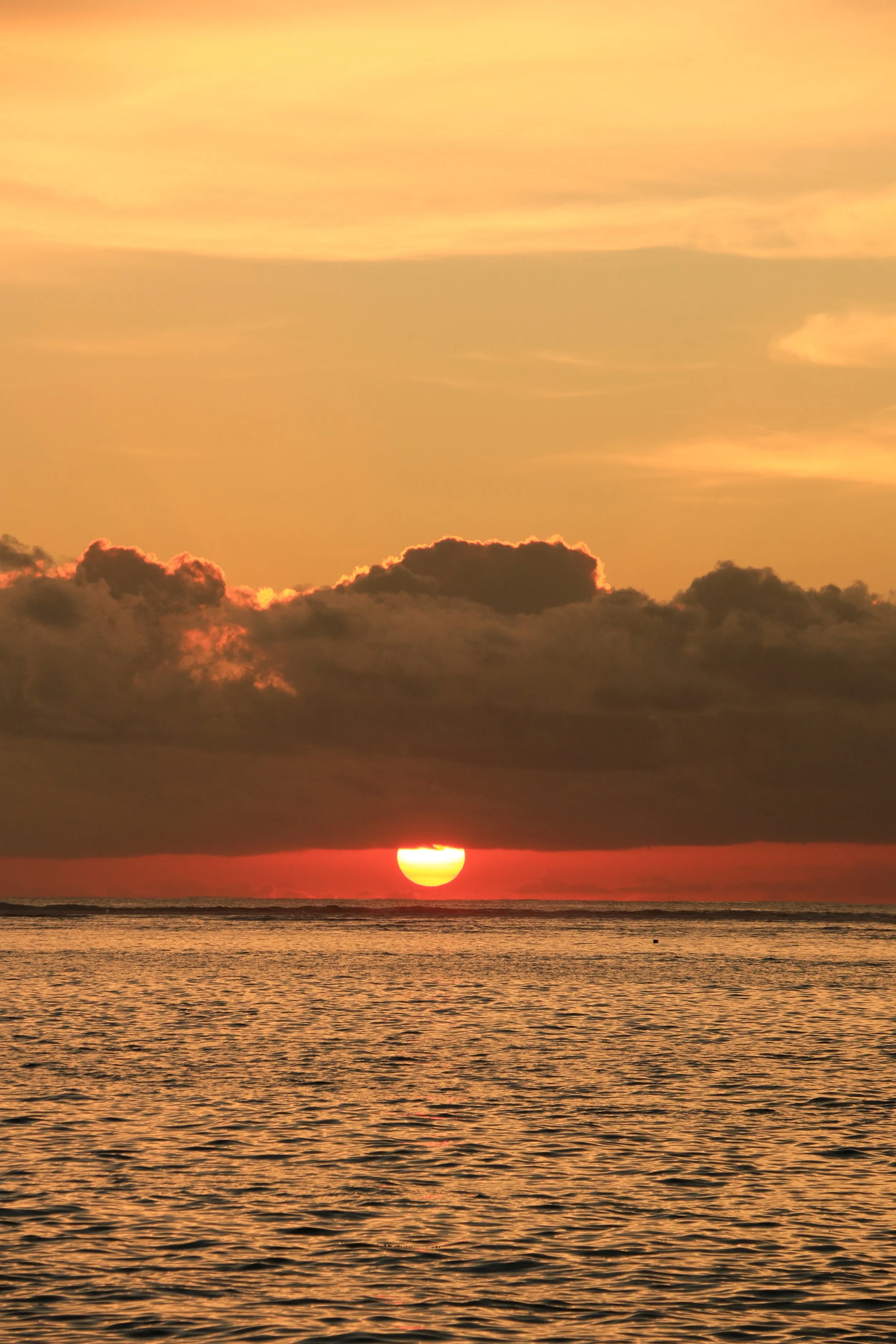 A sunset over the ocean with partly cloudy sky and the sun partially obscured by clouds.