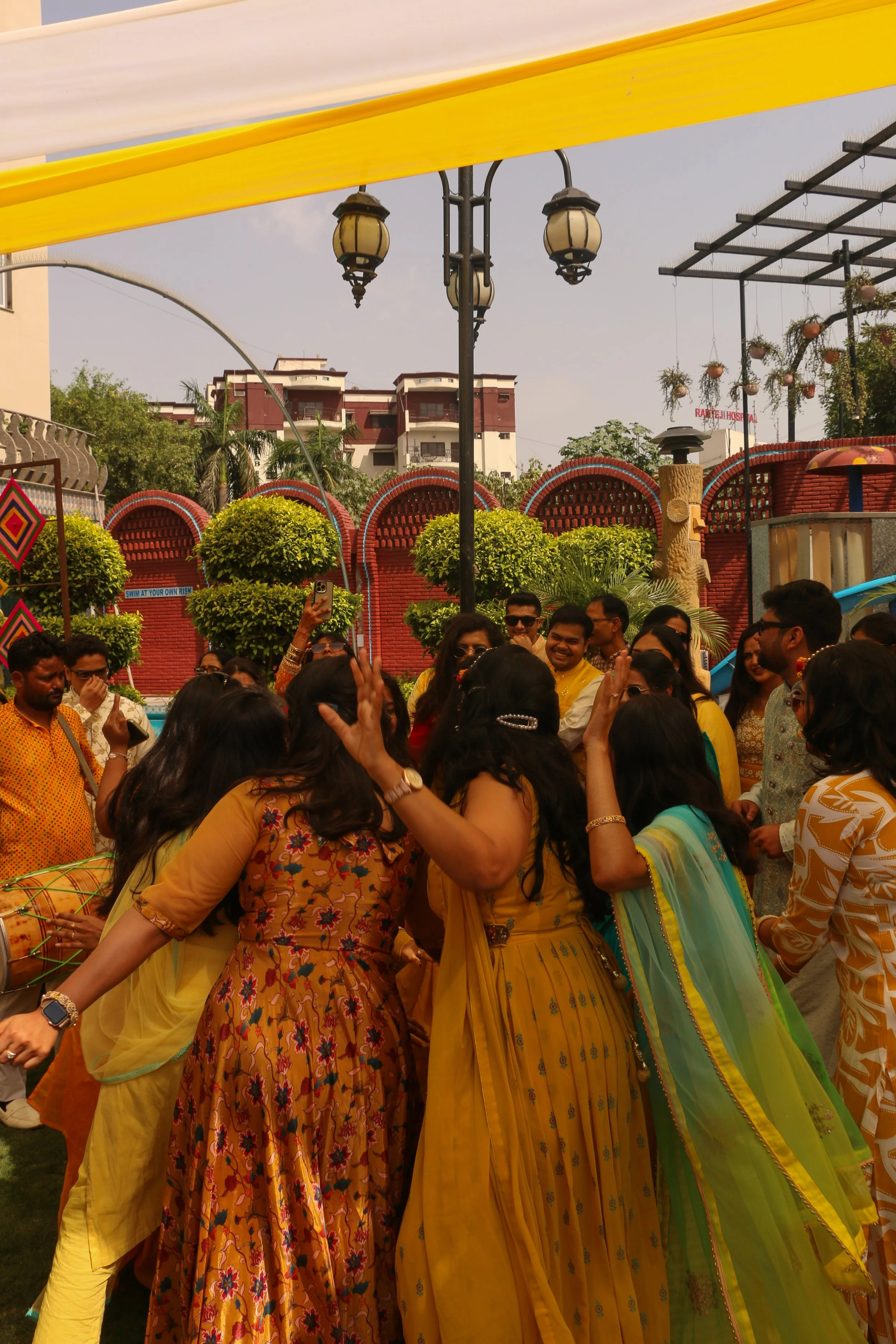 A group of people celebrating, dressed in colorful traditional Indian attire, outdoors during daytime.