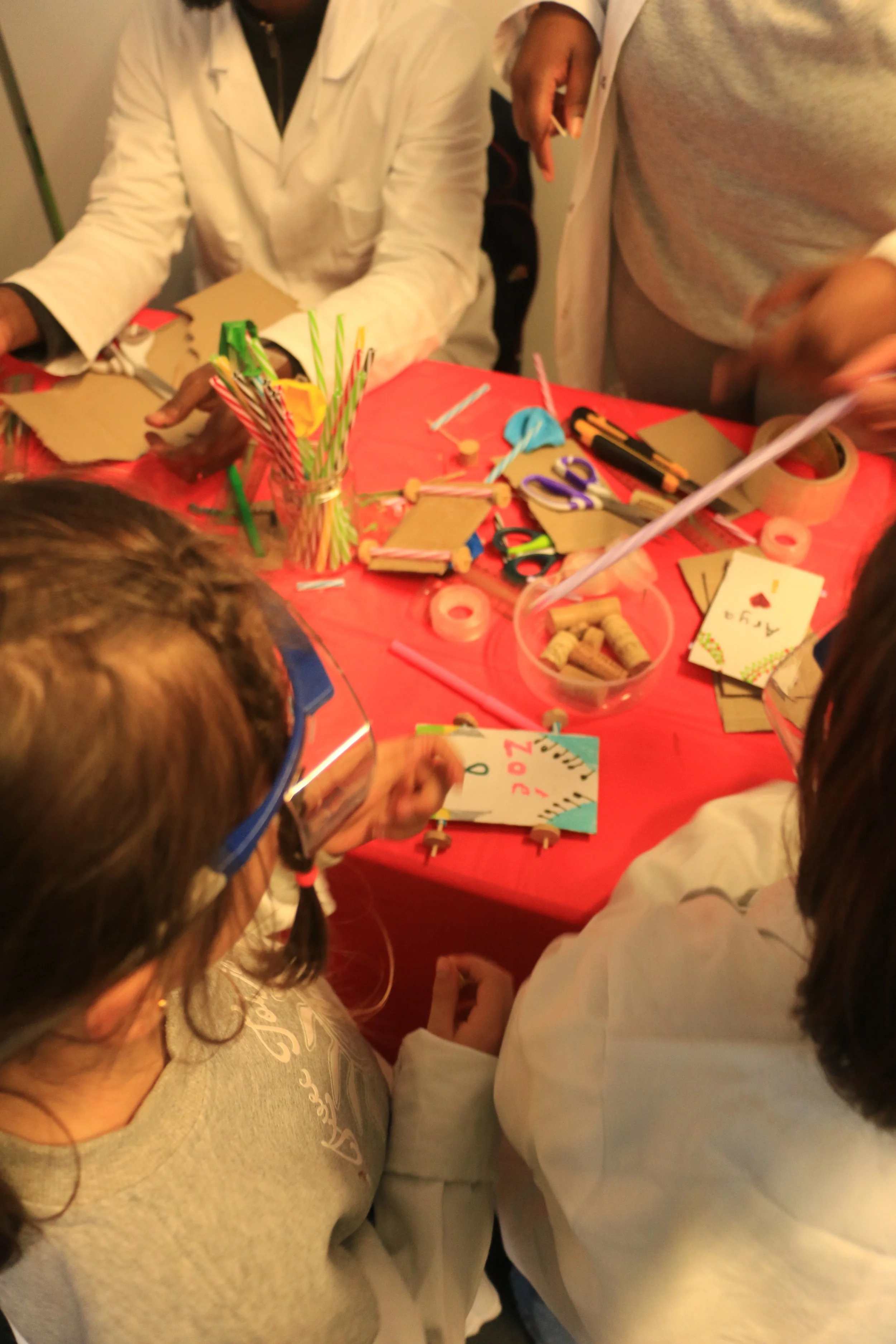 A group of children and adults gathered around a table covered with craft supplies for a holiday card-making activity.