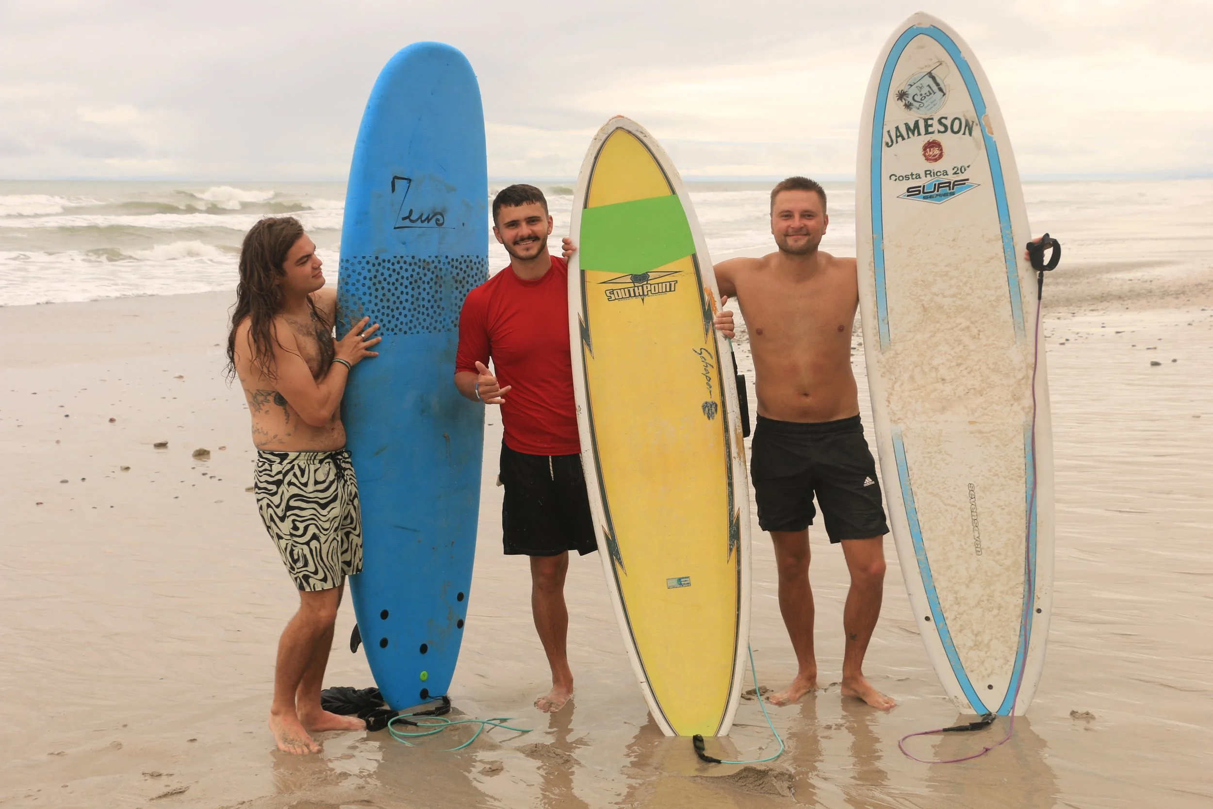 Three people standing on the beach holding surfboards, with the ocean waves in the background.