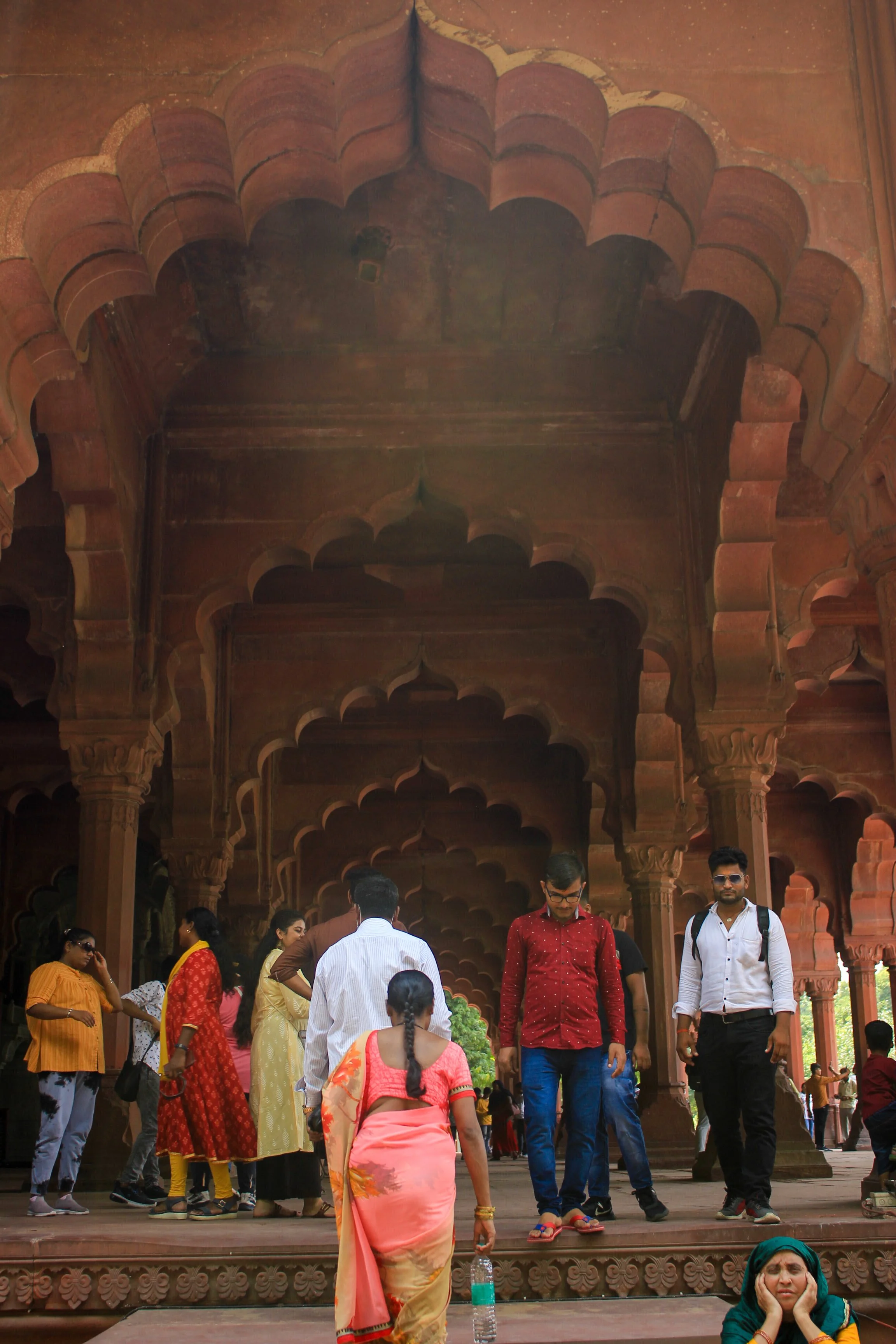 People visiting a historic monument with intricate reddish stone architecture and arches.