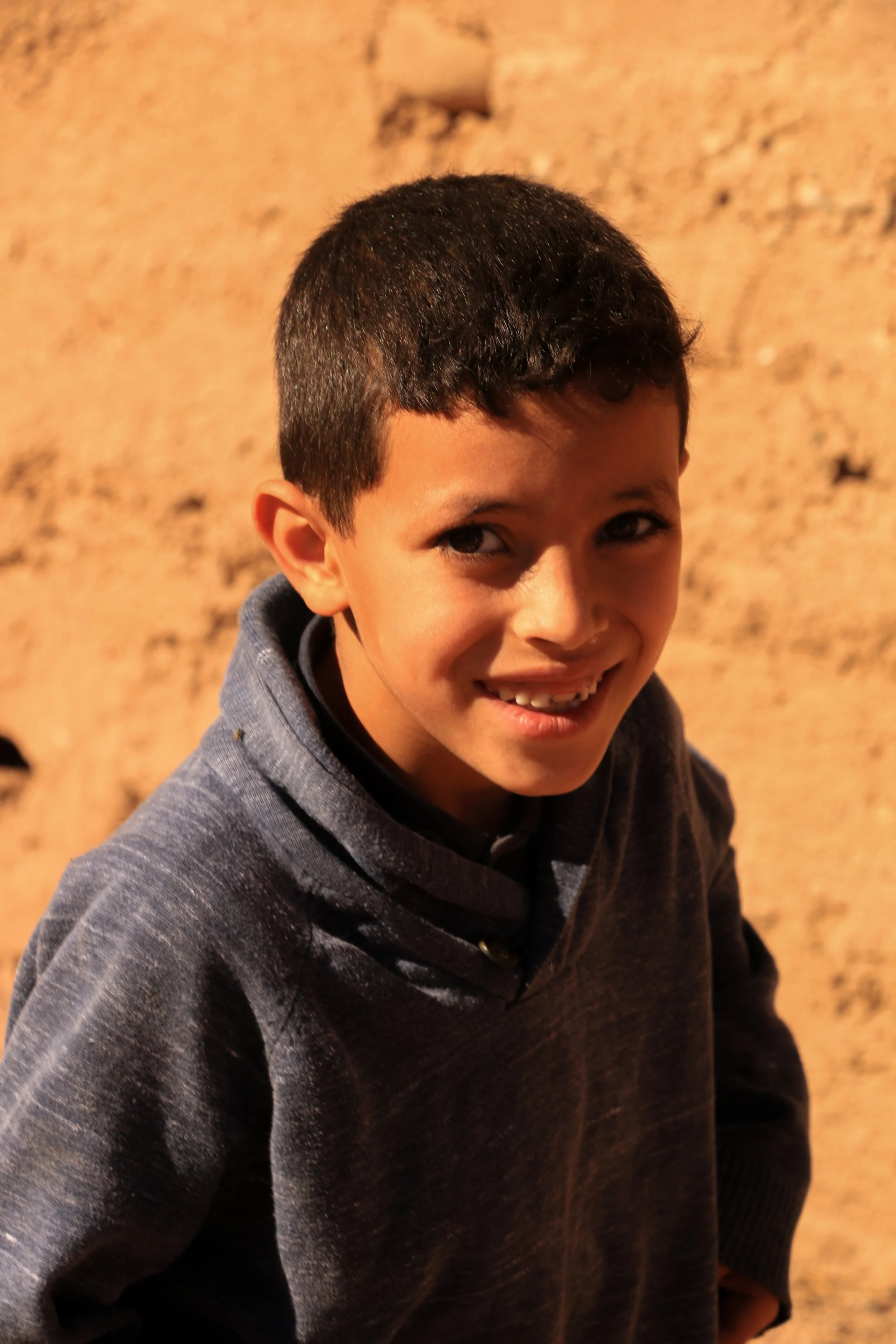 A young boy smiling outdoors at sunset against a rocky background.