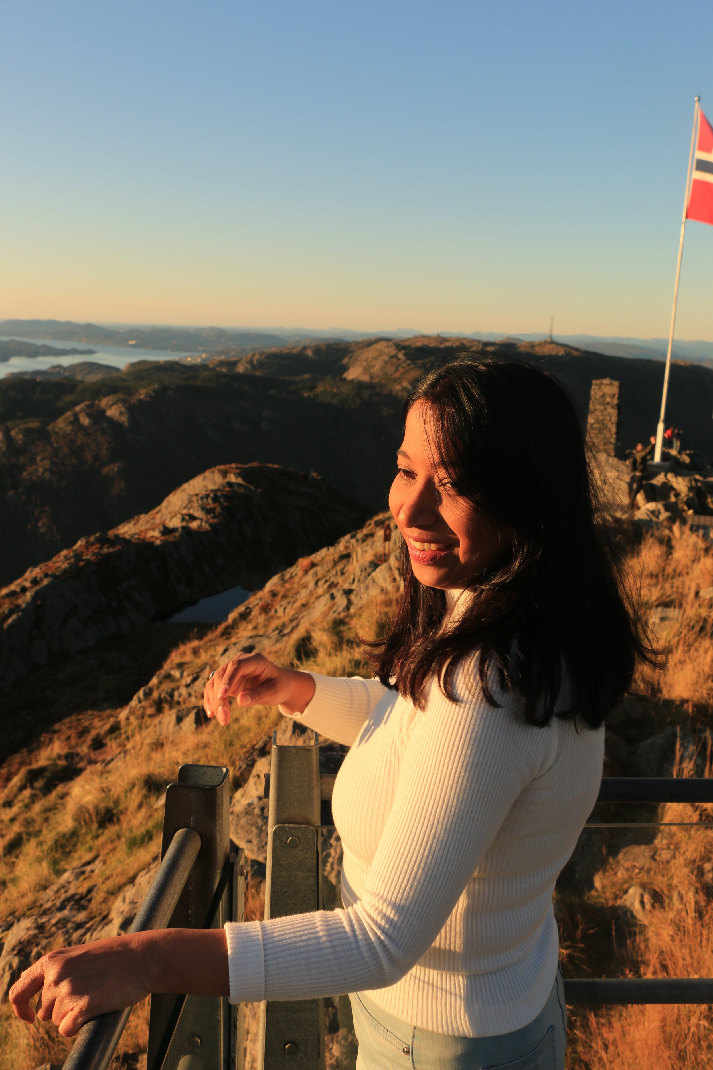 A woman smiling and enjoying the sunset at a mountain overlook with a flag in the background.