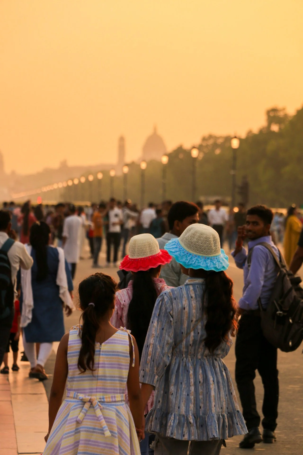 People walking along a city street during sunset, with historic buildings and a dome in the background.