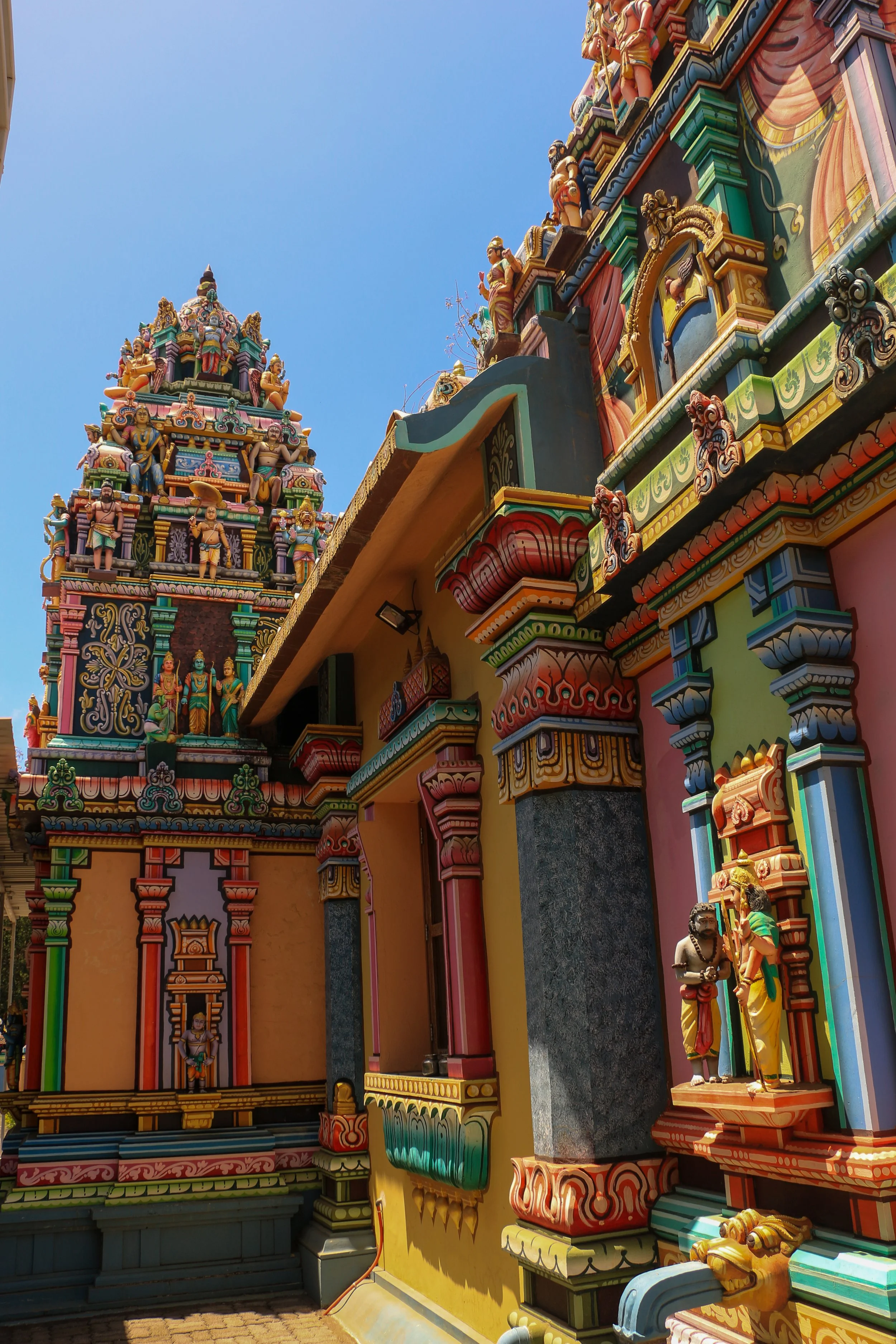 Colorful Hindu temple with intricate carvings and statues of deities against a bright blue sky.