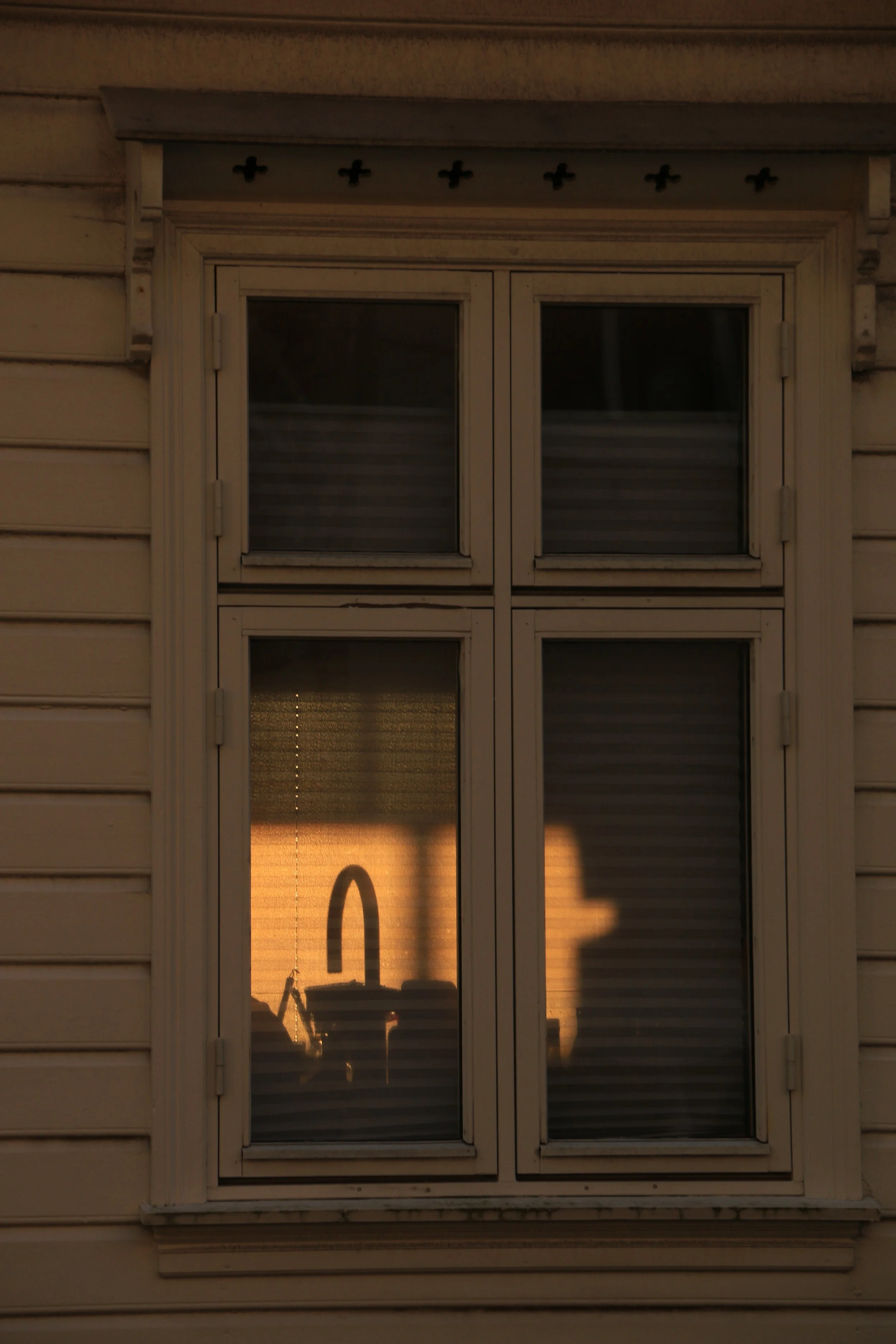 Sunlight reflecting off a window shows the silhouette of a kitchen sink with a high-arc faucet and items on the countertop inside the house.