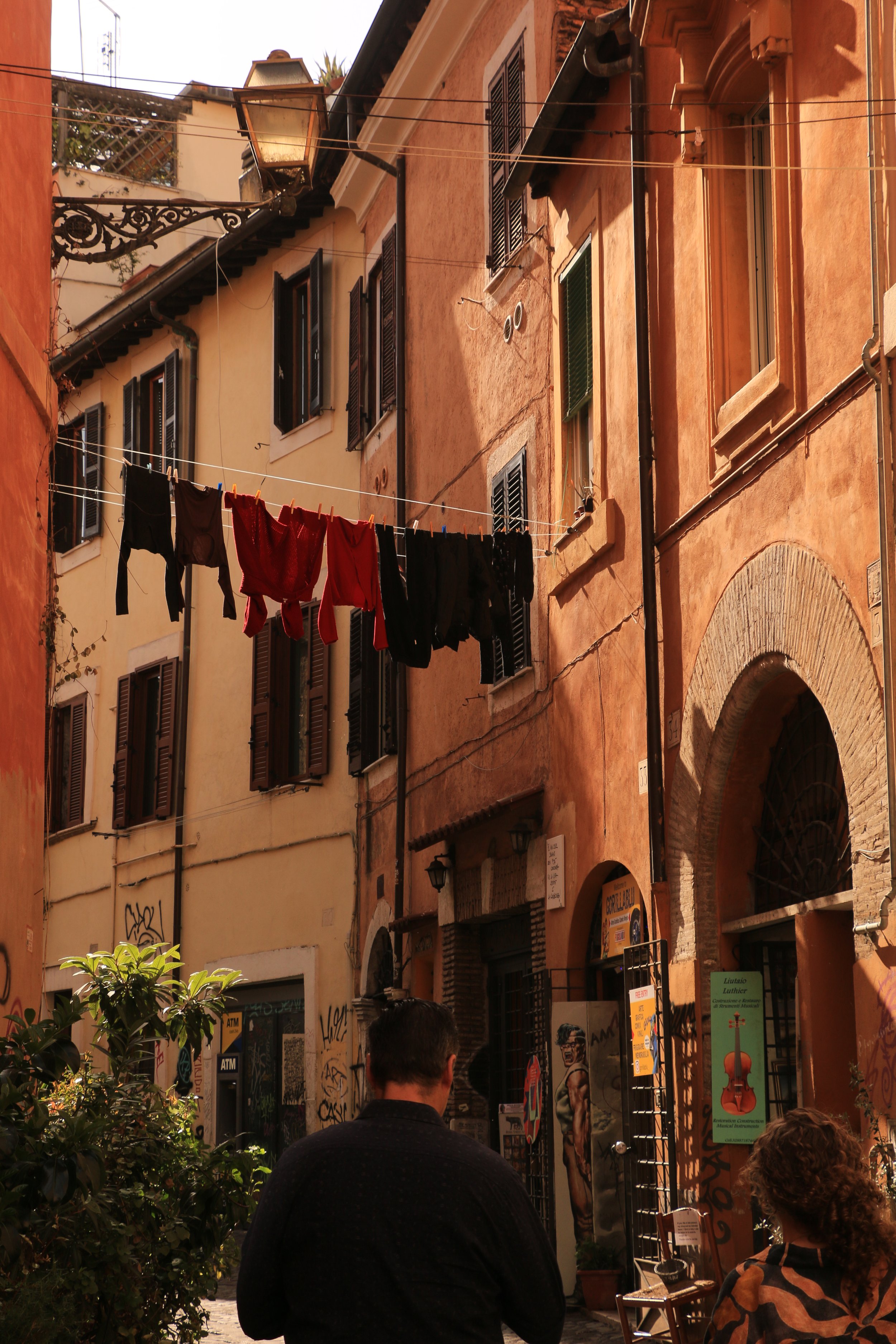 Street scene in Italy with laundry hanging on a line, colorful buildings, and two people walking.