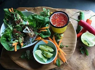 Fresh salad with lettuce wraps, shredded carrots, and vegetables on a wooden board with lime wedges and a cup of chili sauce.