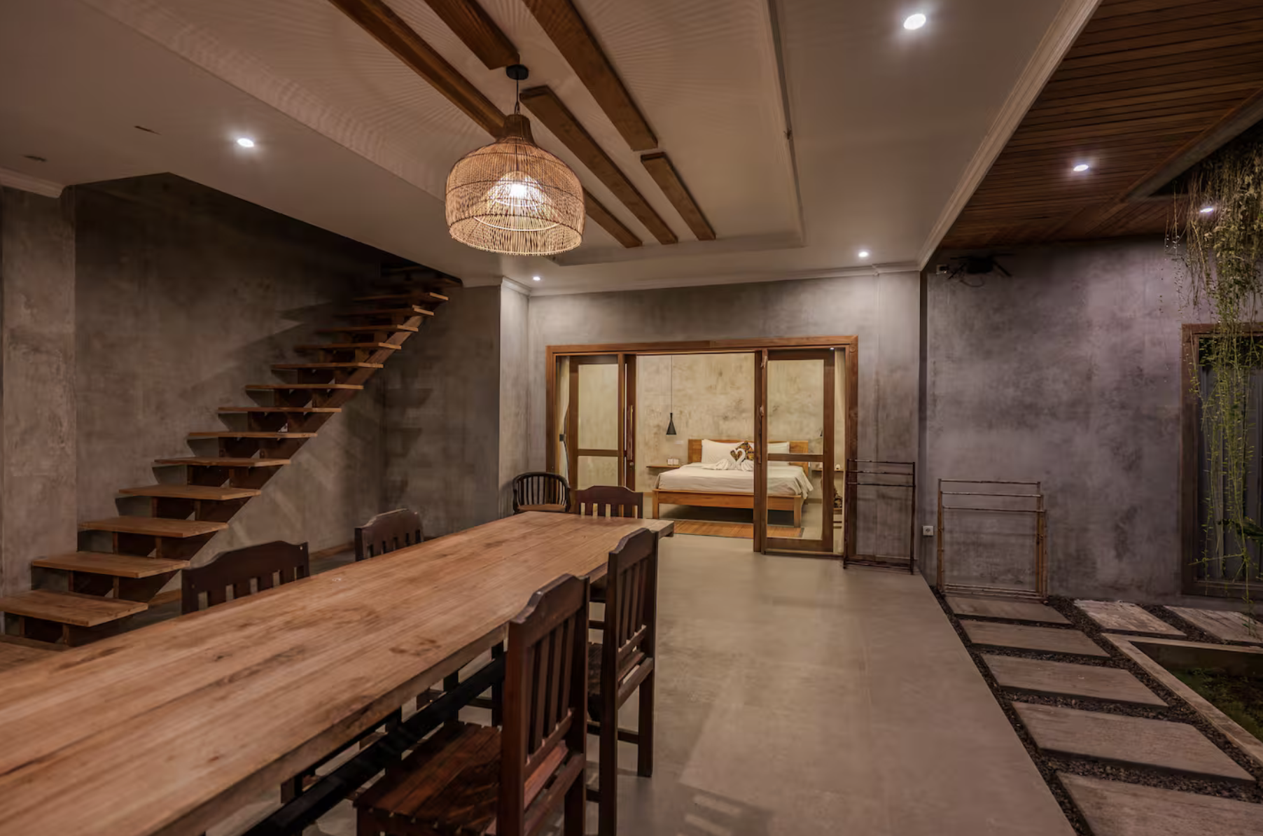Porch with hammock, wooden ceiling beams, light green railing, and hanging wicker light fixture, overlooking lush trees.