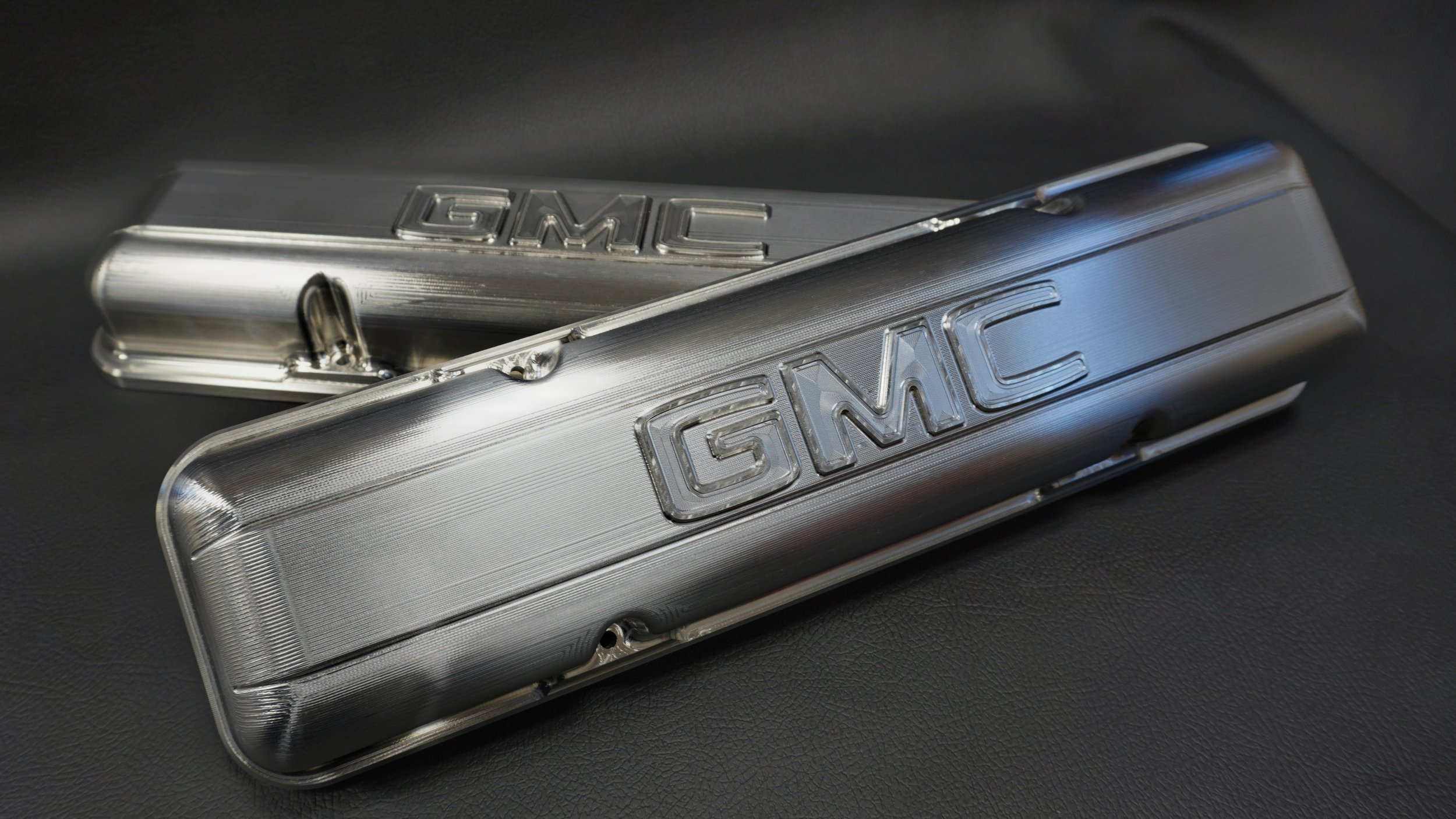 Engineered & tastefully reproduced billet 6061 aluminum GMC engine valve covers with engraved GMC logos, resting on a black surface. A Bad Oman Classics OEM+ billet aluminum product.