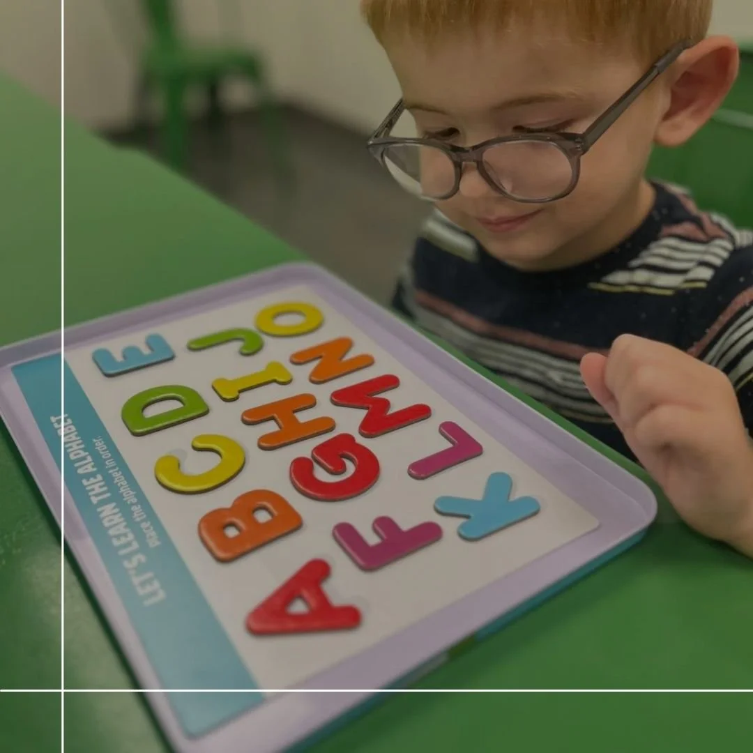 A young boy with glasses looking at a colorful magnetic alphabet puzzle on a table.