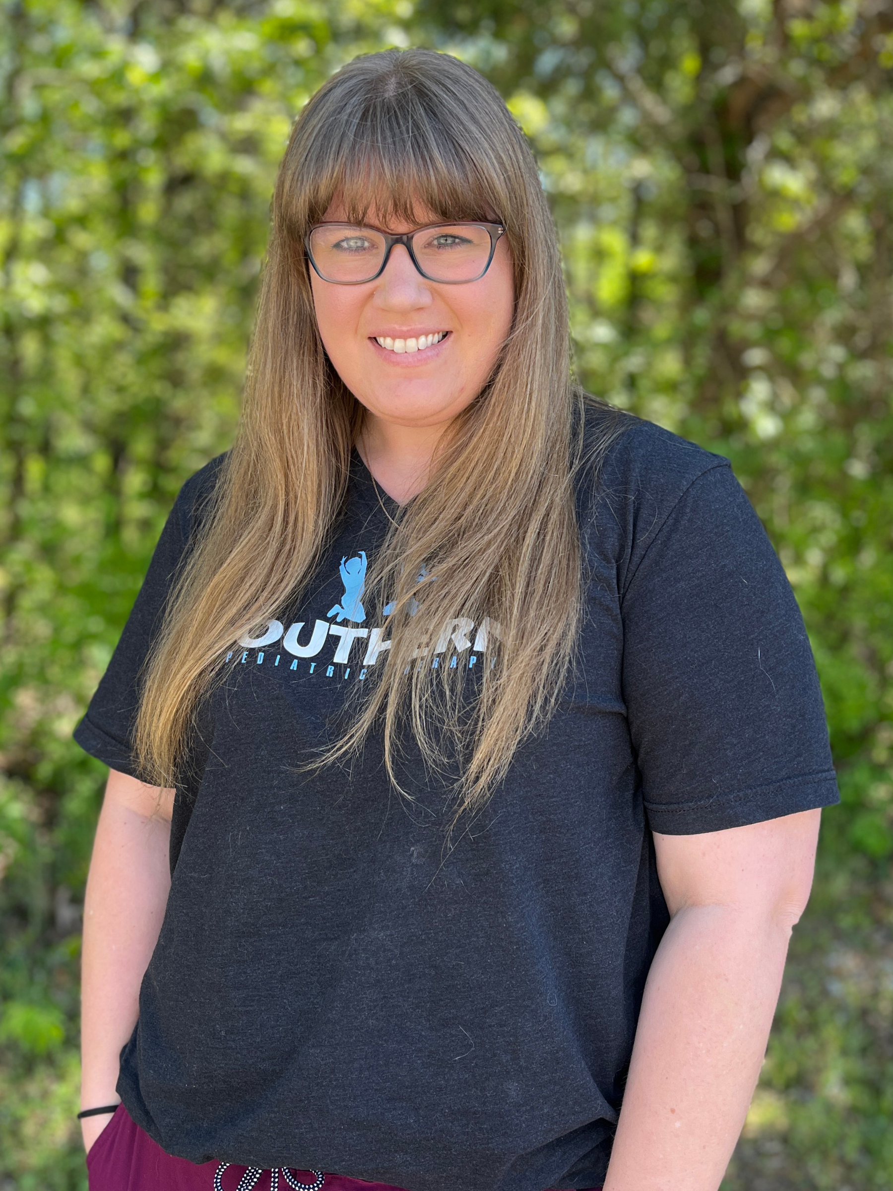 Person with long hair and glasses wearing a black T-shirt outdoors.