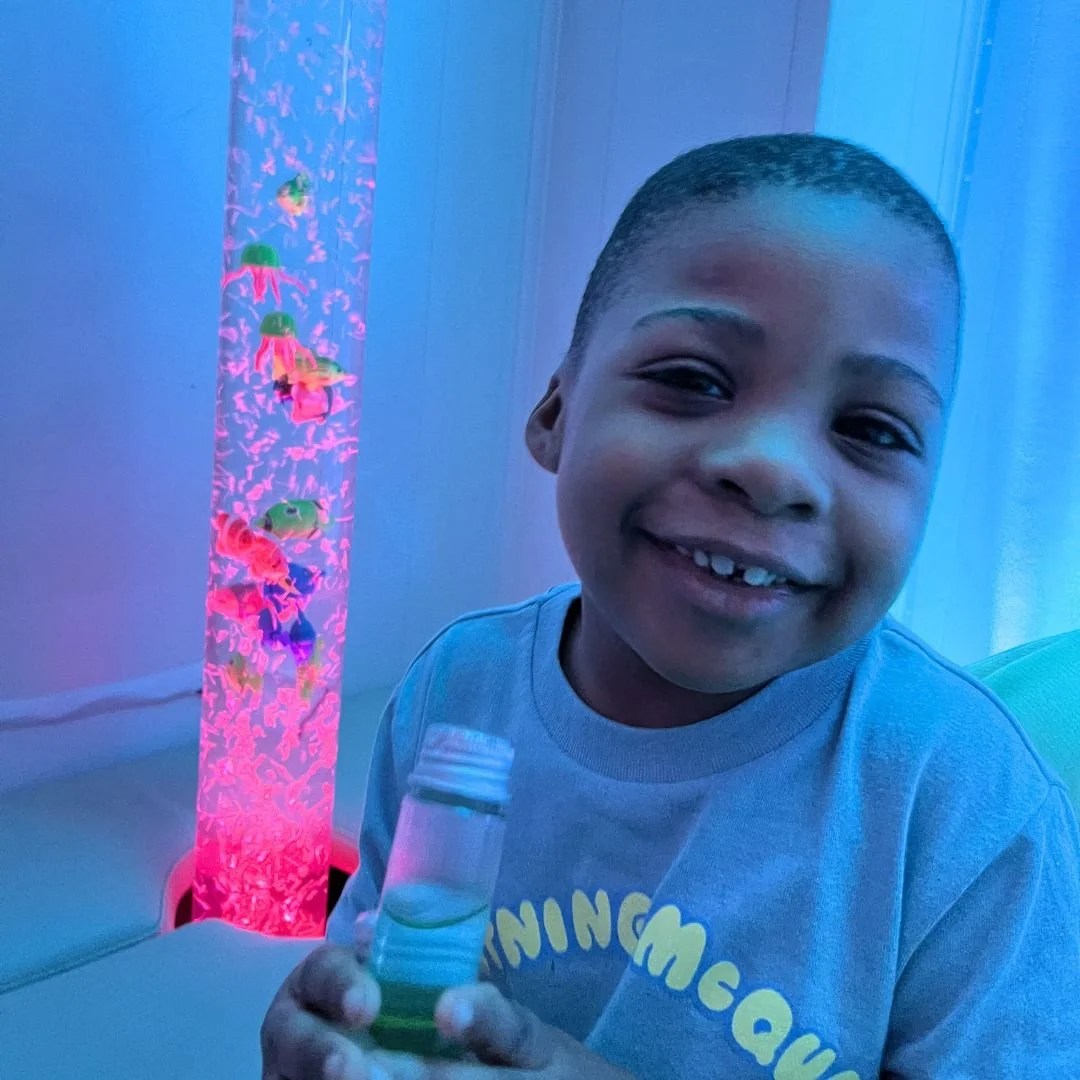 Child smiling in a therapeutic sensory room with colorful fish tank at southern pediatric therapy