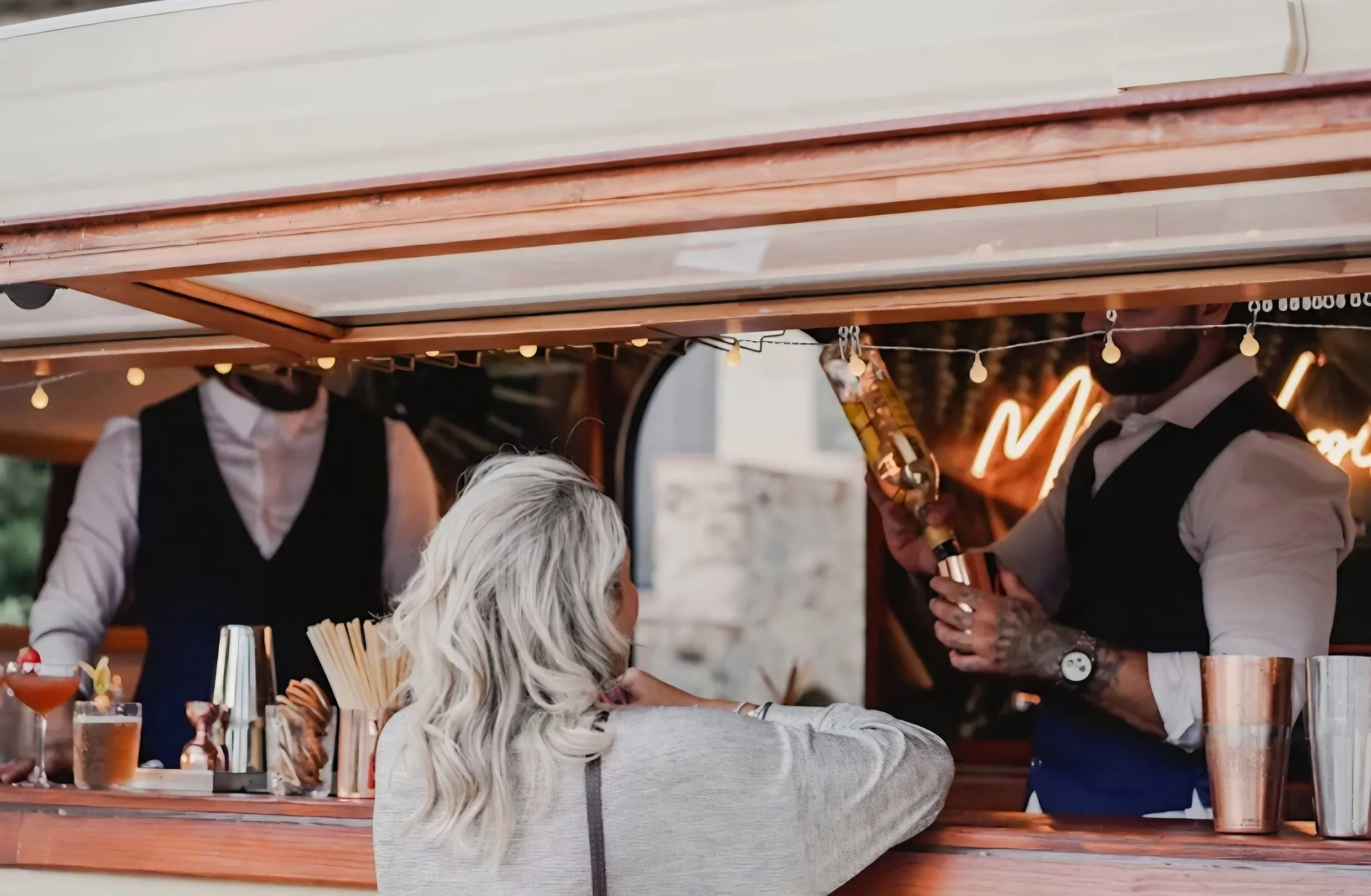 Barman jouant de la flûte dans un bar animé, face à une cliente assise au comptoir.
