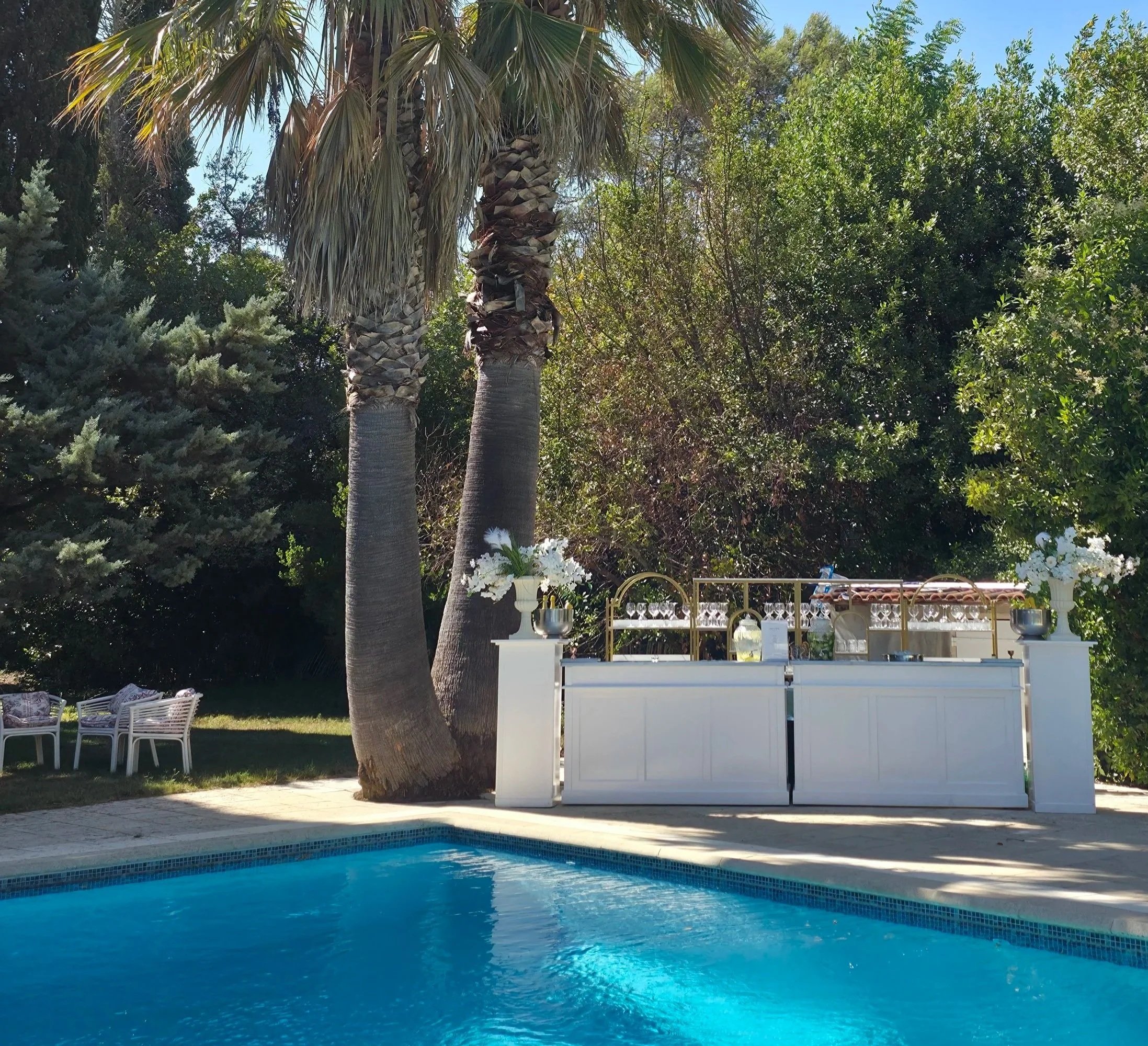 Piscine turquoise en plein air avec une vue sur des palmiers et un mobilier de jardin blanc. Un espace extérieur d'été ensoleillé.