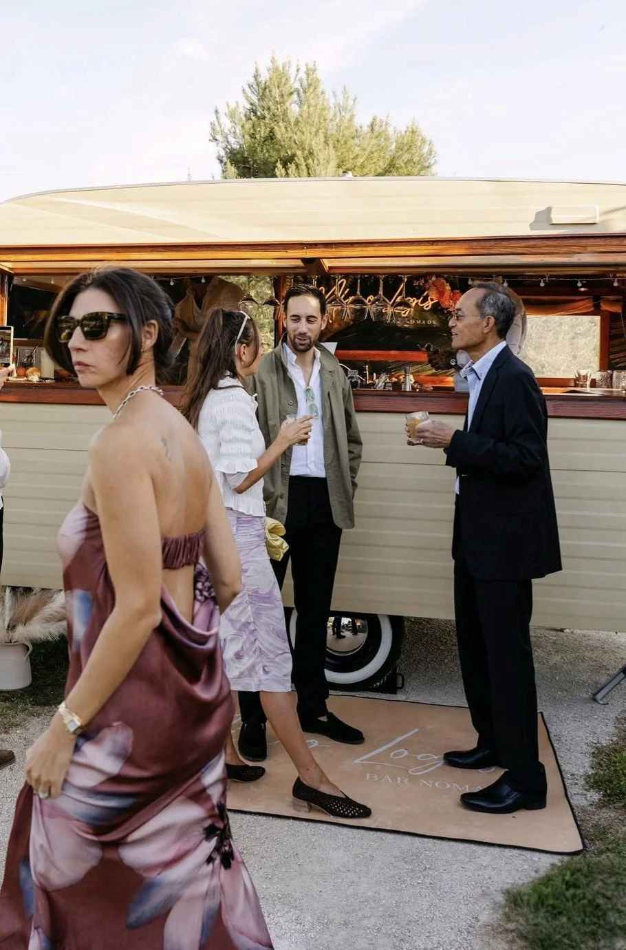 Groupe de personnes discutant devant un stand ou un food truck lors d'un événement en plein air.