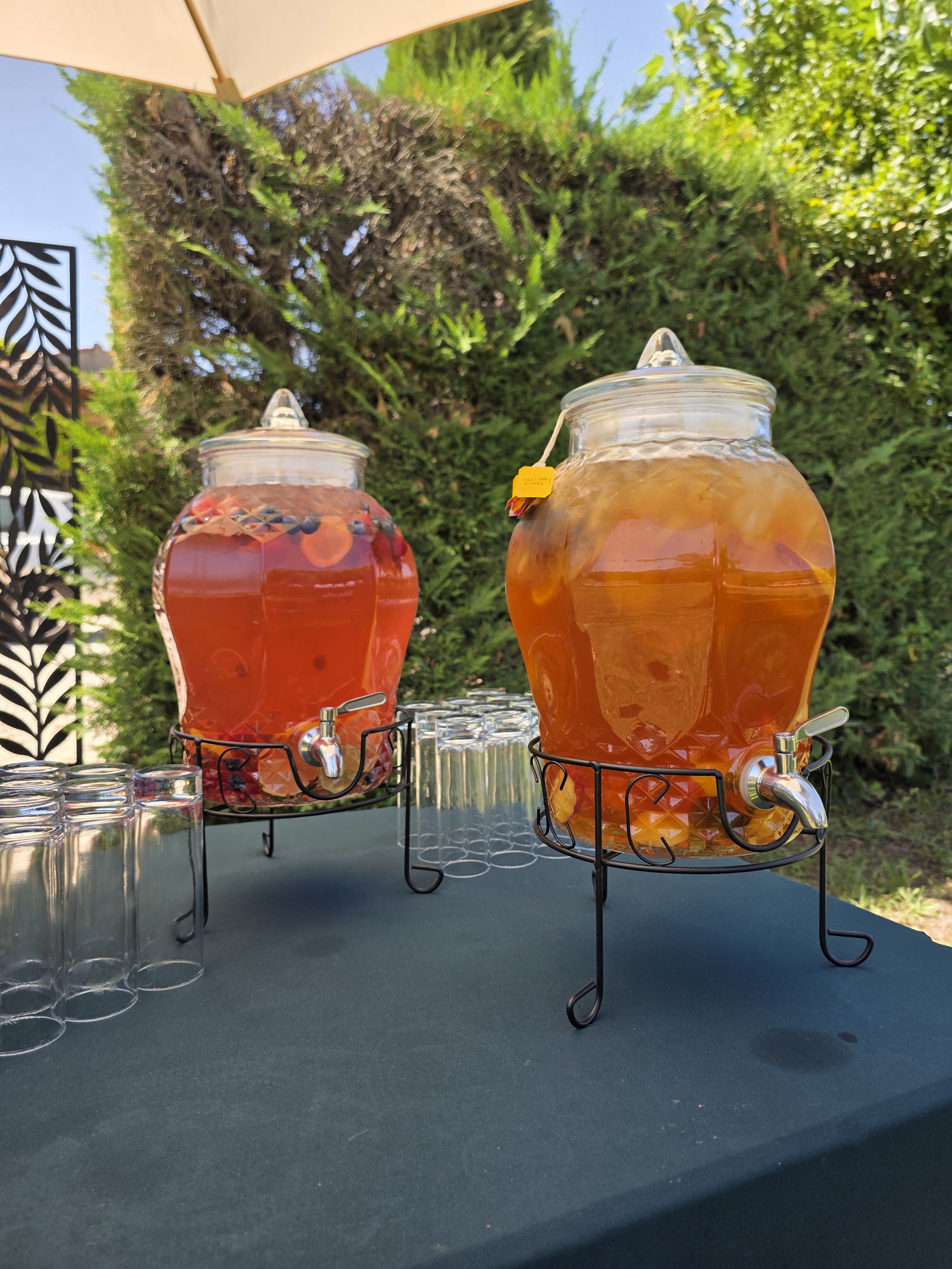 Deux jarres en verre avec des distributeurs de boissons, une à gauche avec une boisson rouge et une à droite avec une boisson orange, placés sur des supports en métal.