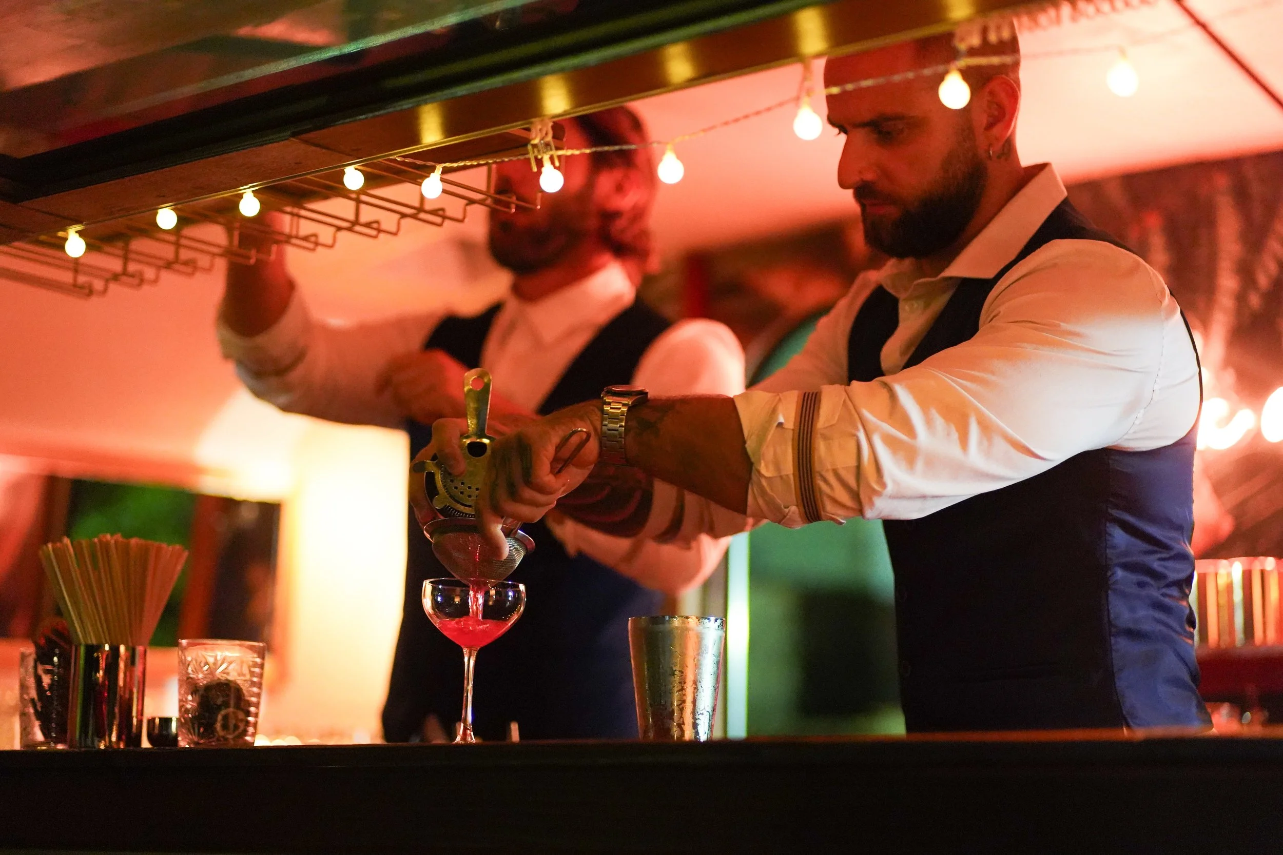 Barman préparant un cocktail dans un bar éclairé de guirlandes lumineuses.