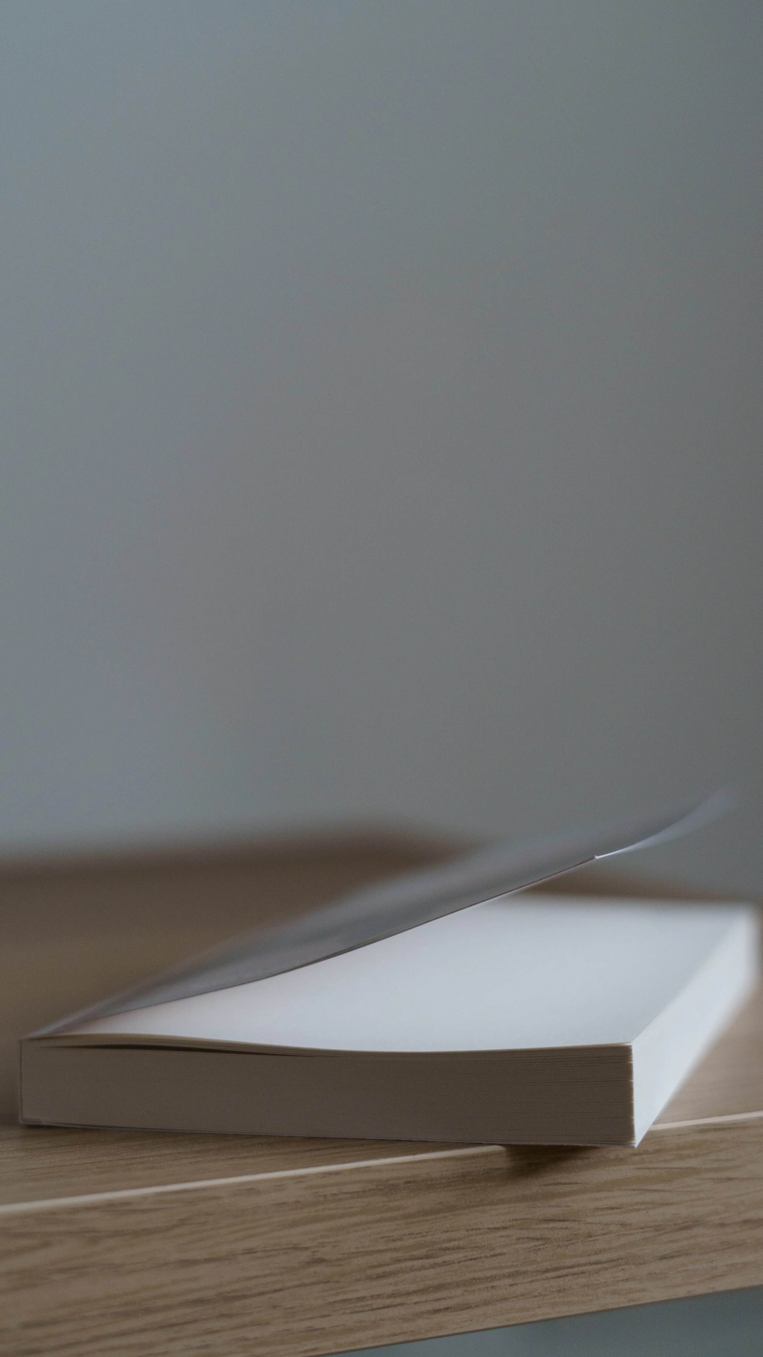 Ein offenes Buch auf einem Holztisch, mit einer schräg aufgestellten Seite. Der Hintergrund ist unscharf und grau.