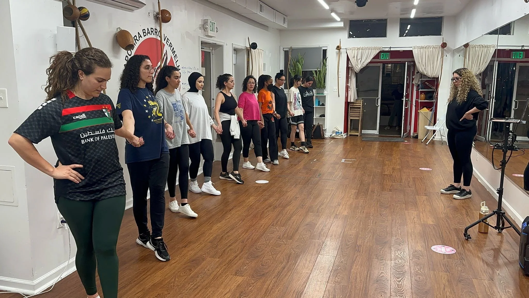 A group of women standing in line inside a fitness studio, with one woman appearing to be instructing or speaking to them.