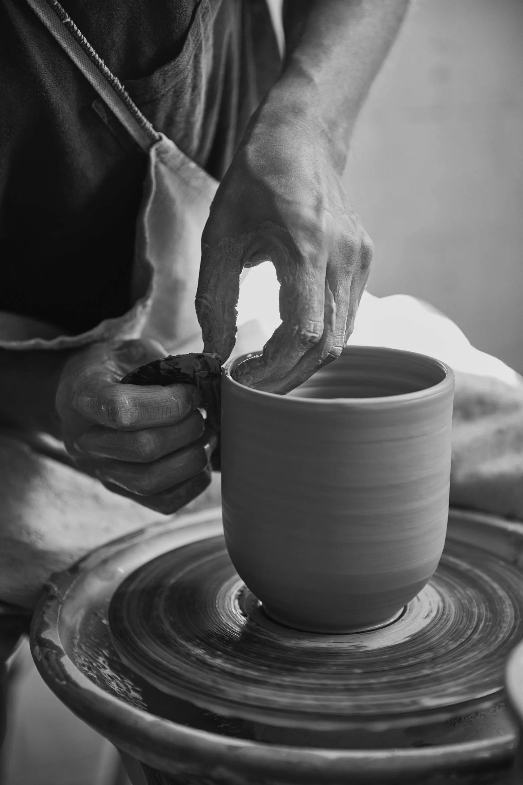 A person shaping a clay pottery piece on a pottery wheel in a ceramic studio, with hands covered in clay and focused on the spinning clay.